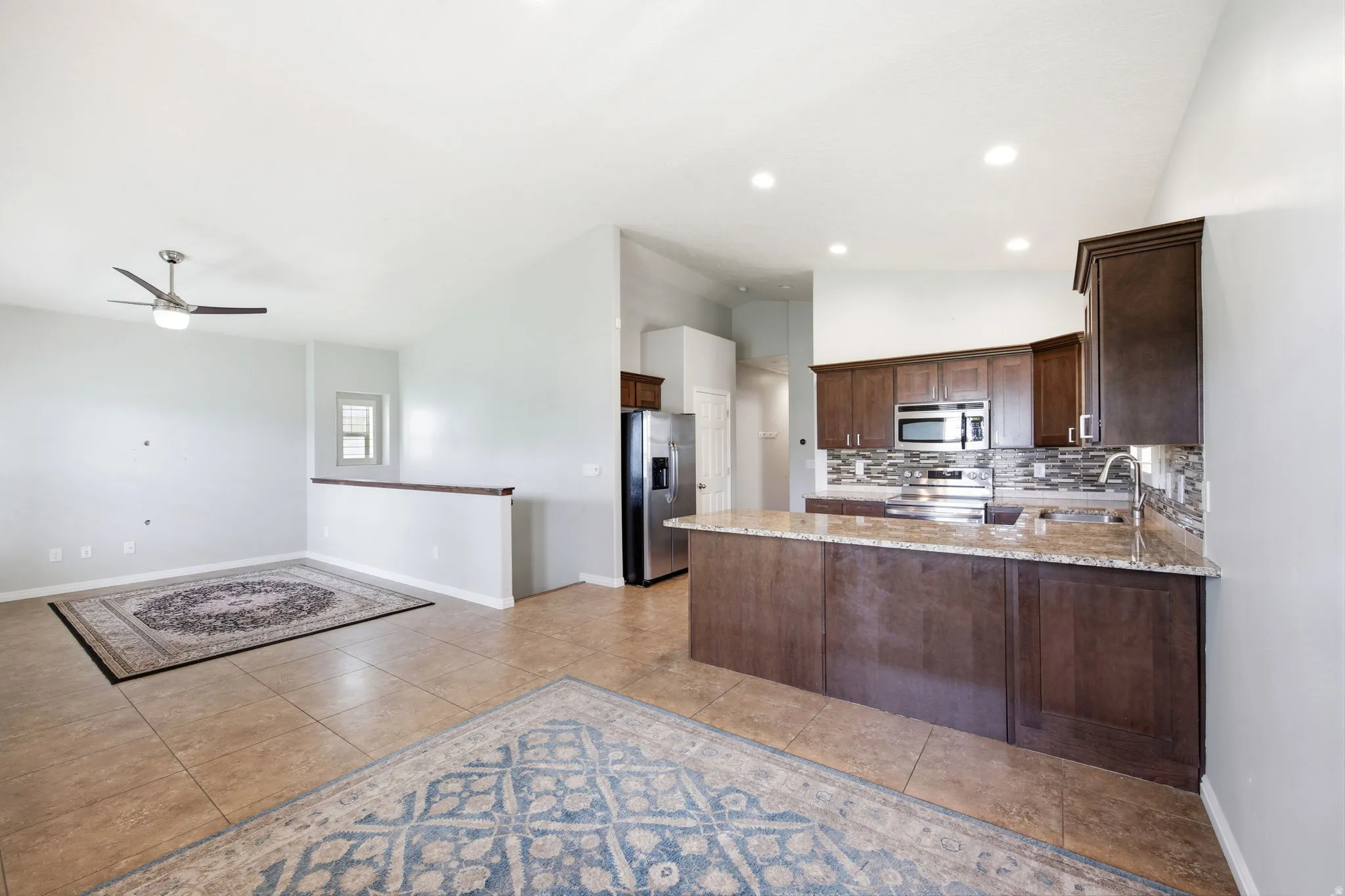 Open-concept kitchen and living area featuring tile flooring, vaulted ceilings, recessed lighting, and a modern ceiling fan