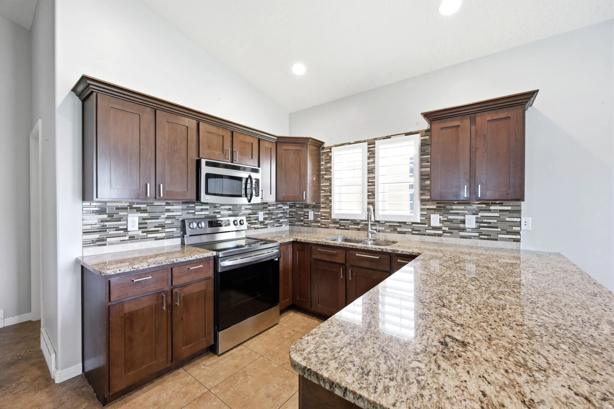 Kitchen featuring abundant wood cabinetry, stainless steel appliances, a multi-tone tile backsplash, light-toned countertops, and a built-in sink with a gooseneck faucet