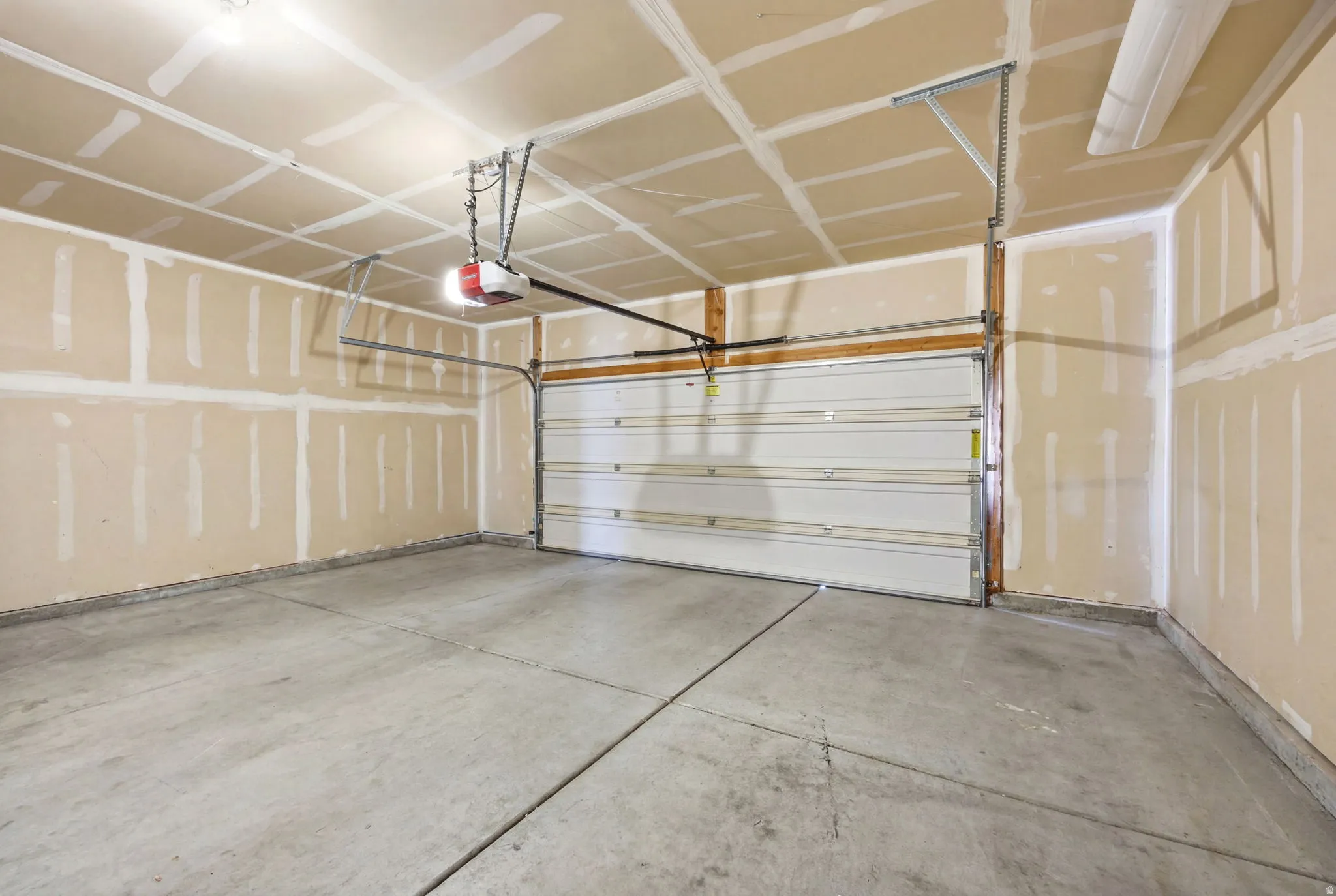 Spacious two-car garage featuring a concrete floor, an overhead garage door opener, and unfinished drywall walls ready for customization