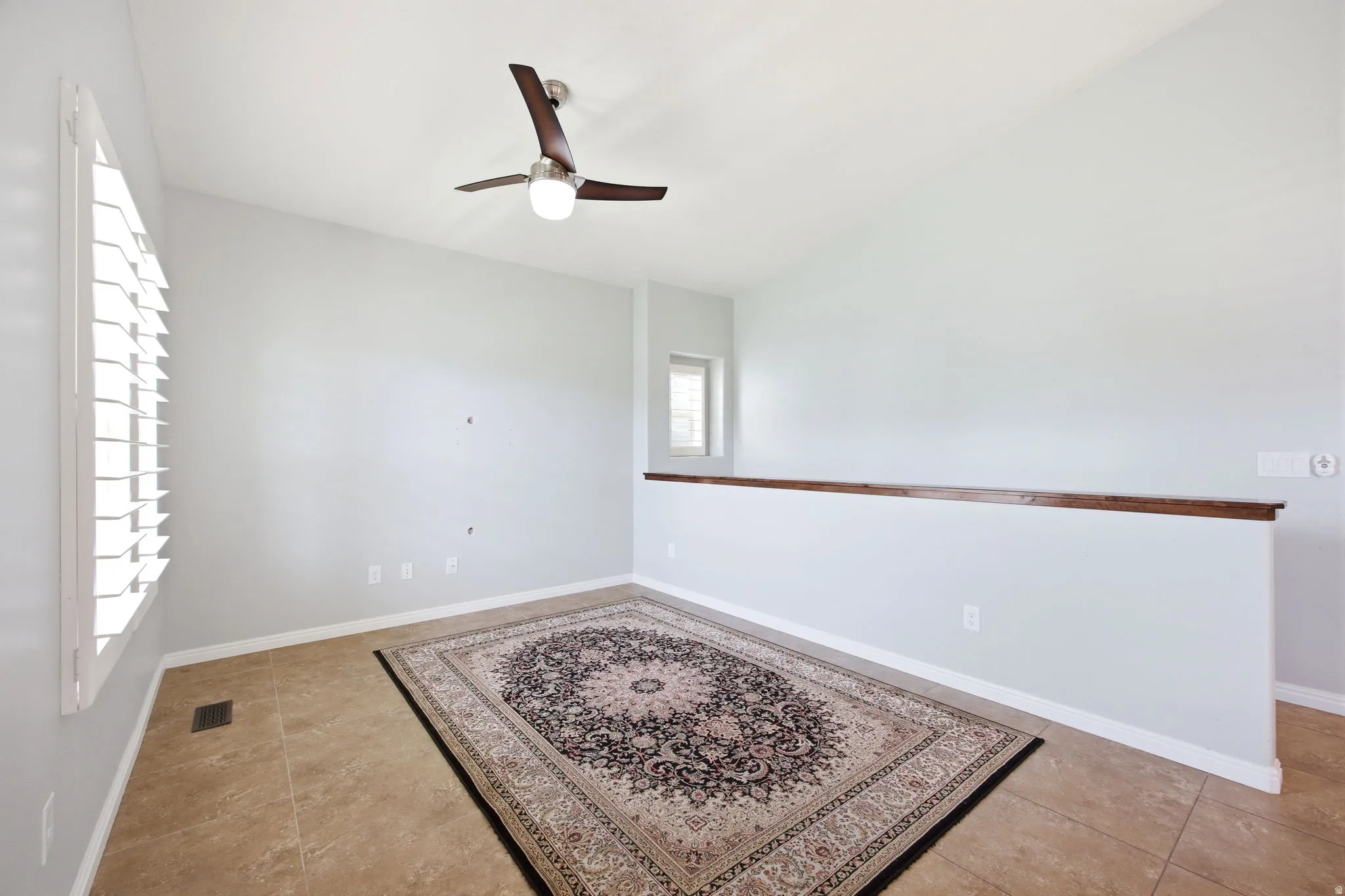 Spacious room featuring neutral paint, ceramic tile flooring, a modern ceiling fan, and plantation shutters
