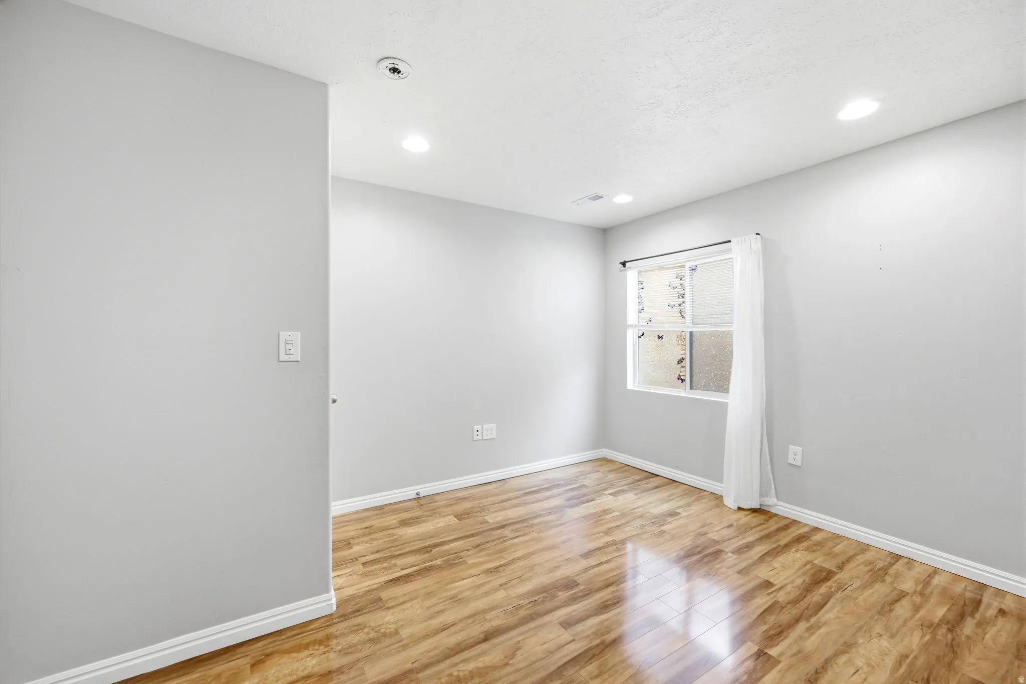 Room featuring wood-finish flooring, recessed lighting, and a window with blinds and a sheer curtain