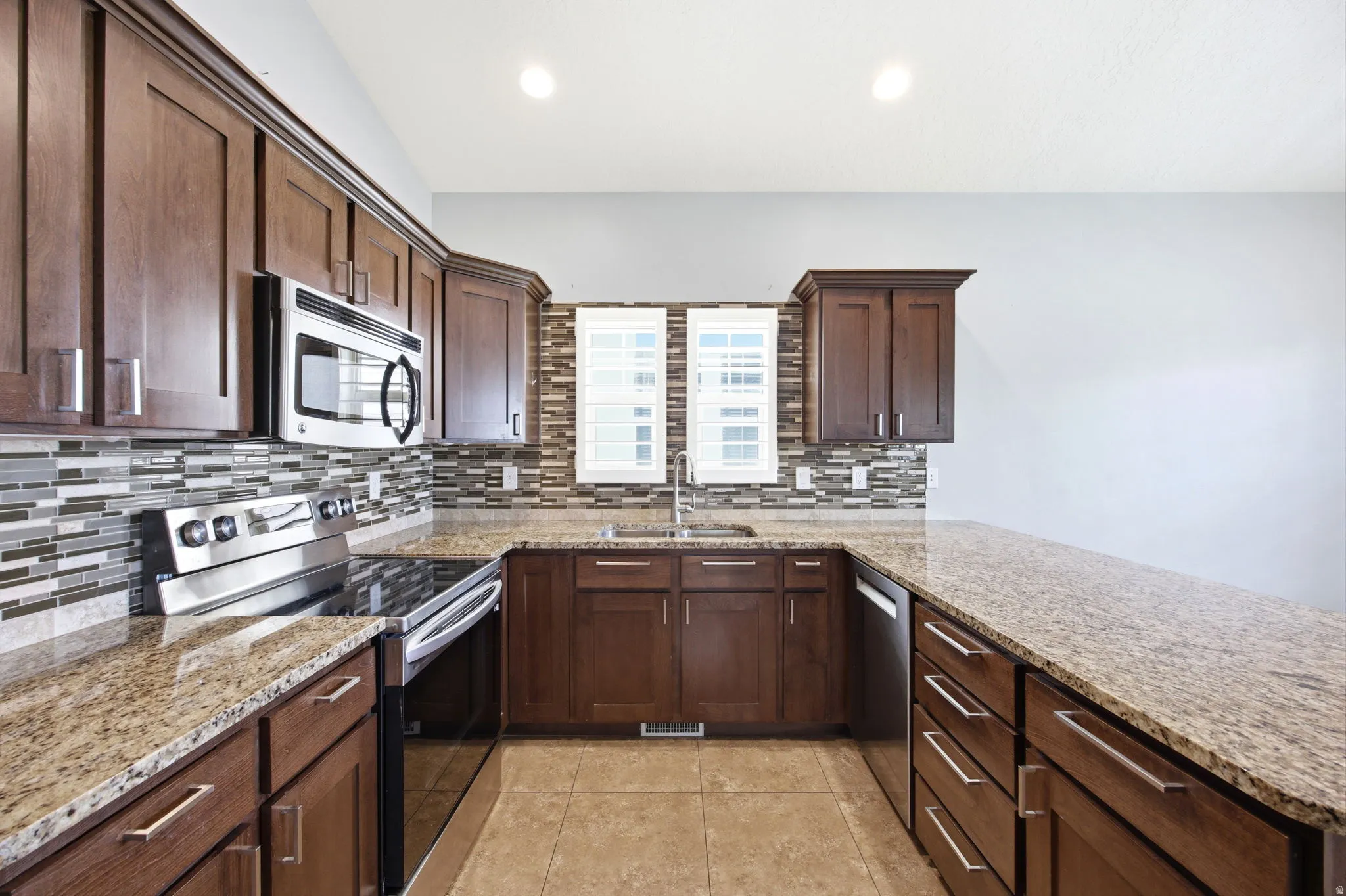 Kitchen featuring dark wood-finish cabinetry, speckled granite countertops, and a mosaic tile backsplash