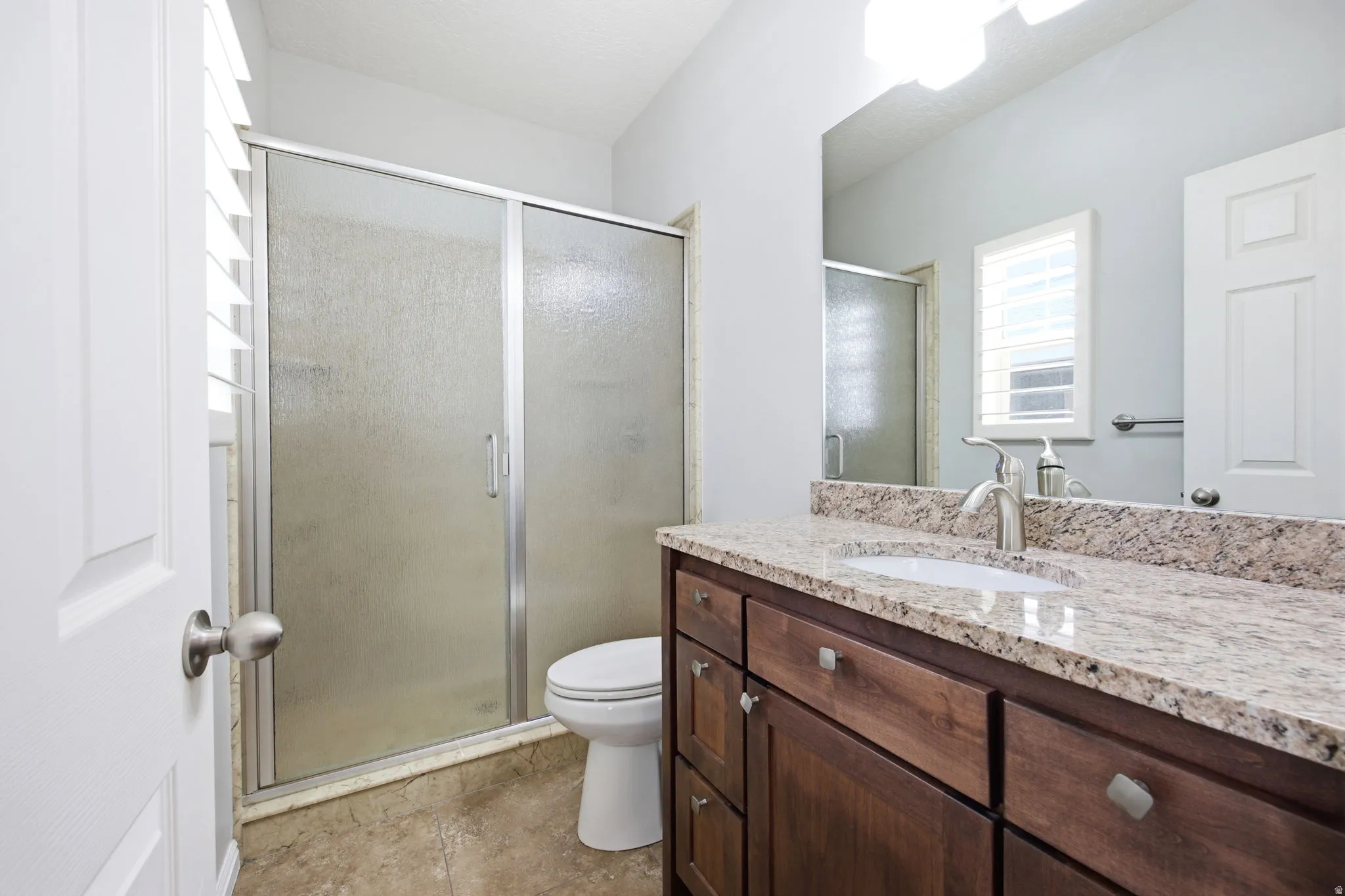 Bathroom featuring a shower with a sliding frosted glass door, a toilet, a vanity with wood cabinetry, a light-toned countertop, and a built-in sink