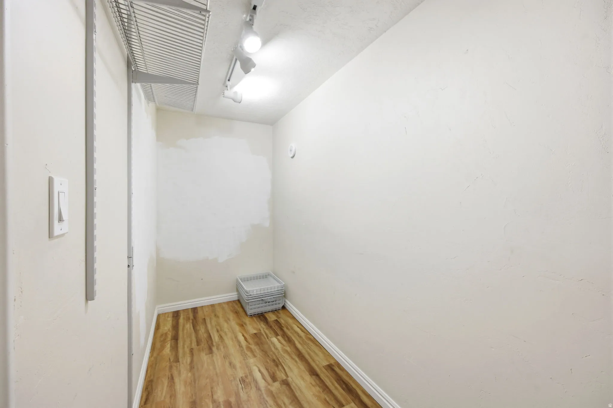 Storage area featuring wood-finish flooring, white baseboards, and track lighting