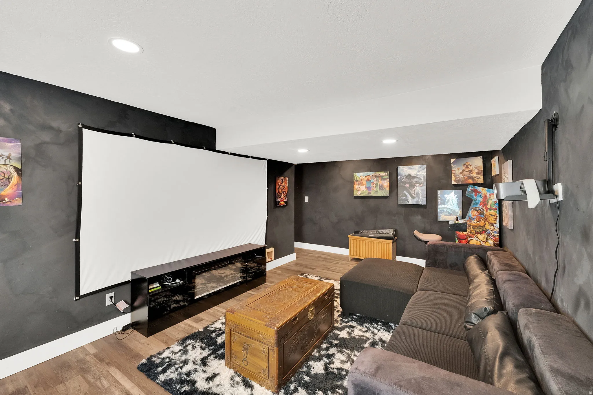 Dedicated entertainment space featuring a large projection screen, built-in media console, recessed lighting, wood-finish flooring, and dark textured wall finishes