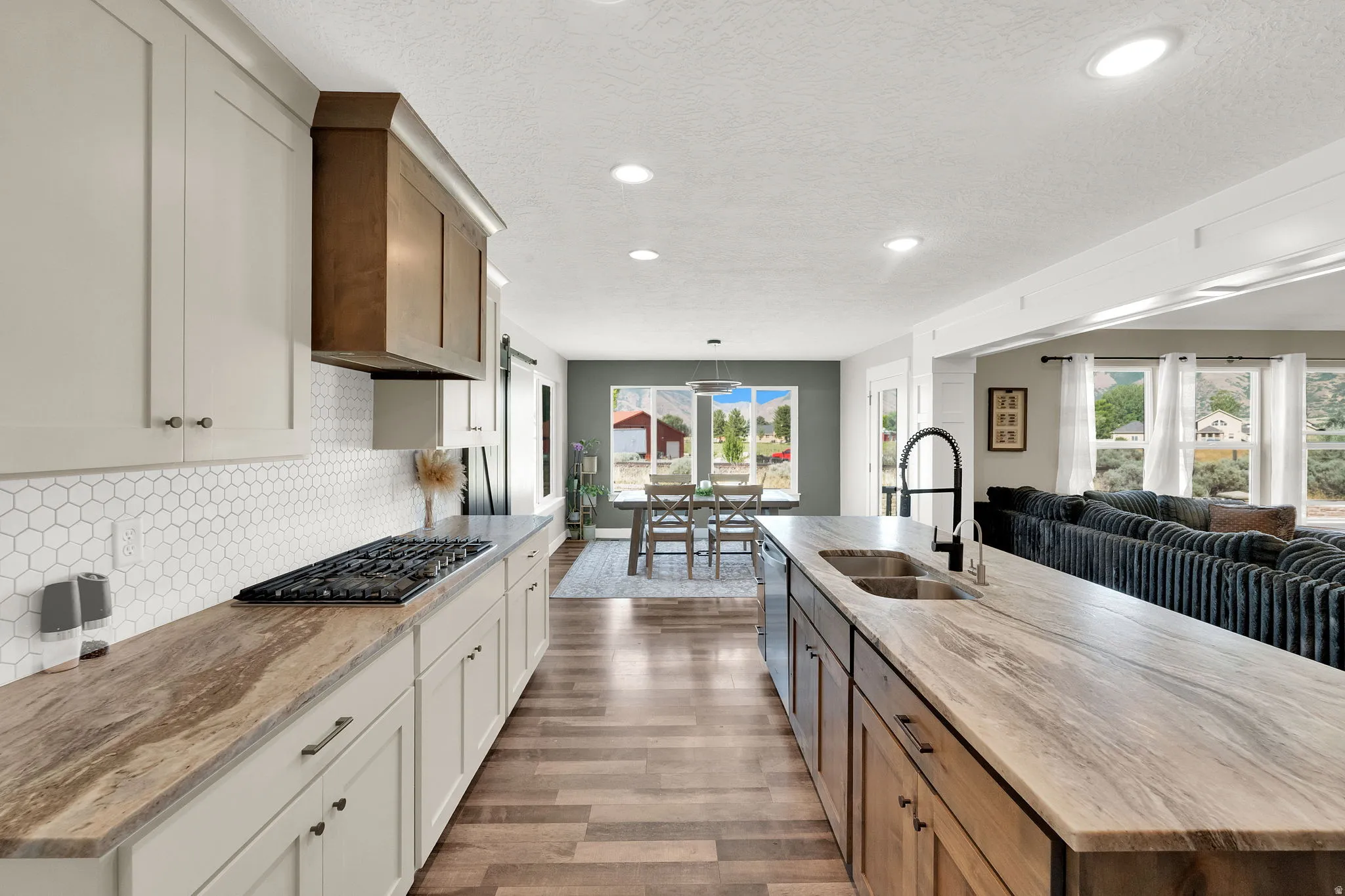 Gourmet kitchen featuring a gas cooktop, white hexagonal tile backsplash, custom range hood, and a large central island with an undermount sink and black faucet