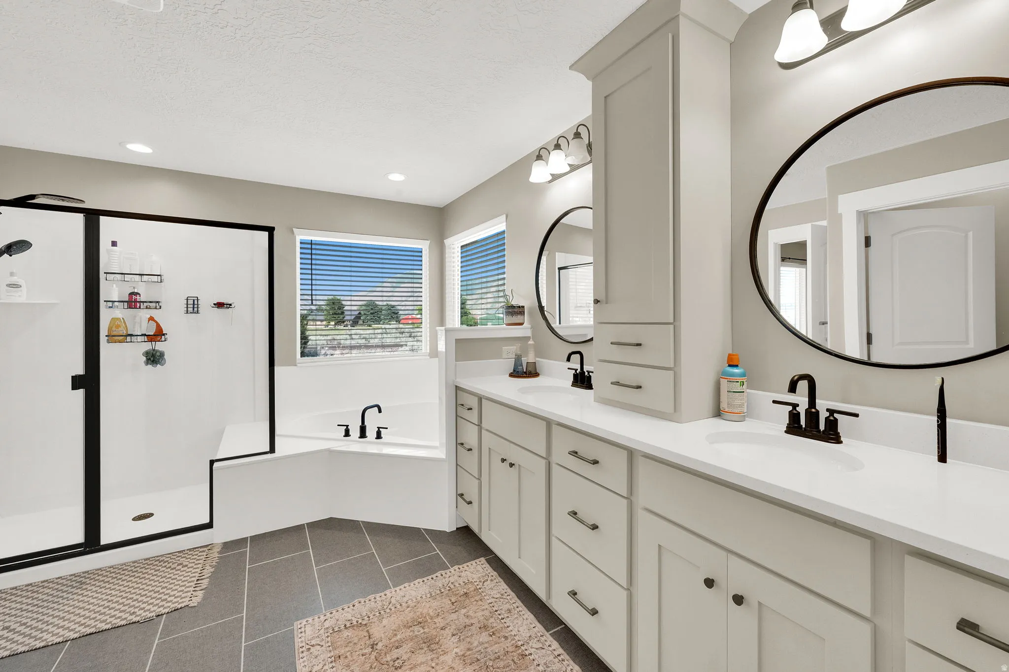 Spacious bathroom featuring a dual vanity with light cabinetry, white countertops, and circular framed mirrors