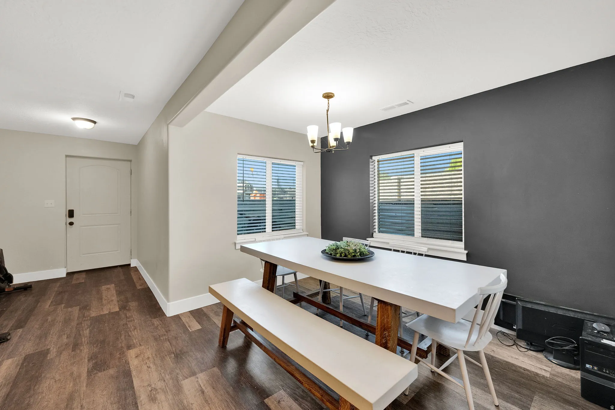 Dining area featuring a dark accent wall, two windows with horizontal blinds, and wood-finish flooring