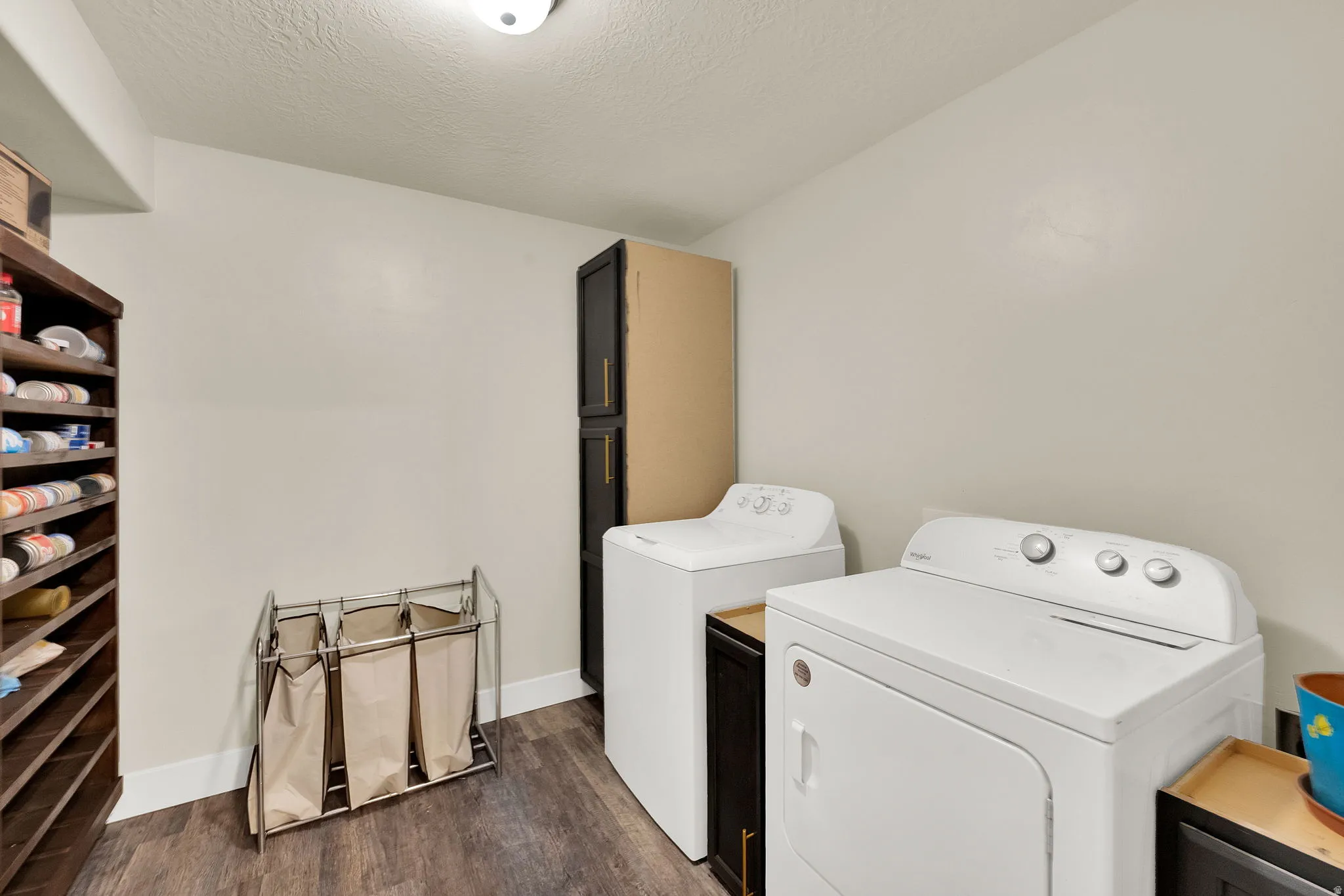Dedicated laundry area featuring wood-finish flooring, white walls, built-in shelving, and dark cabinetry