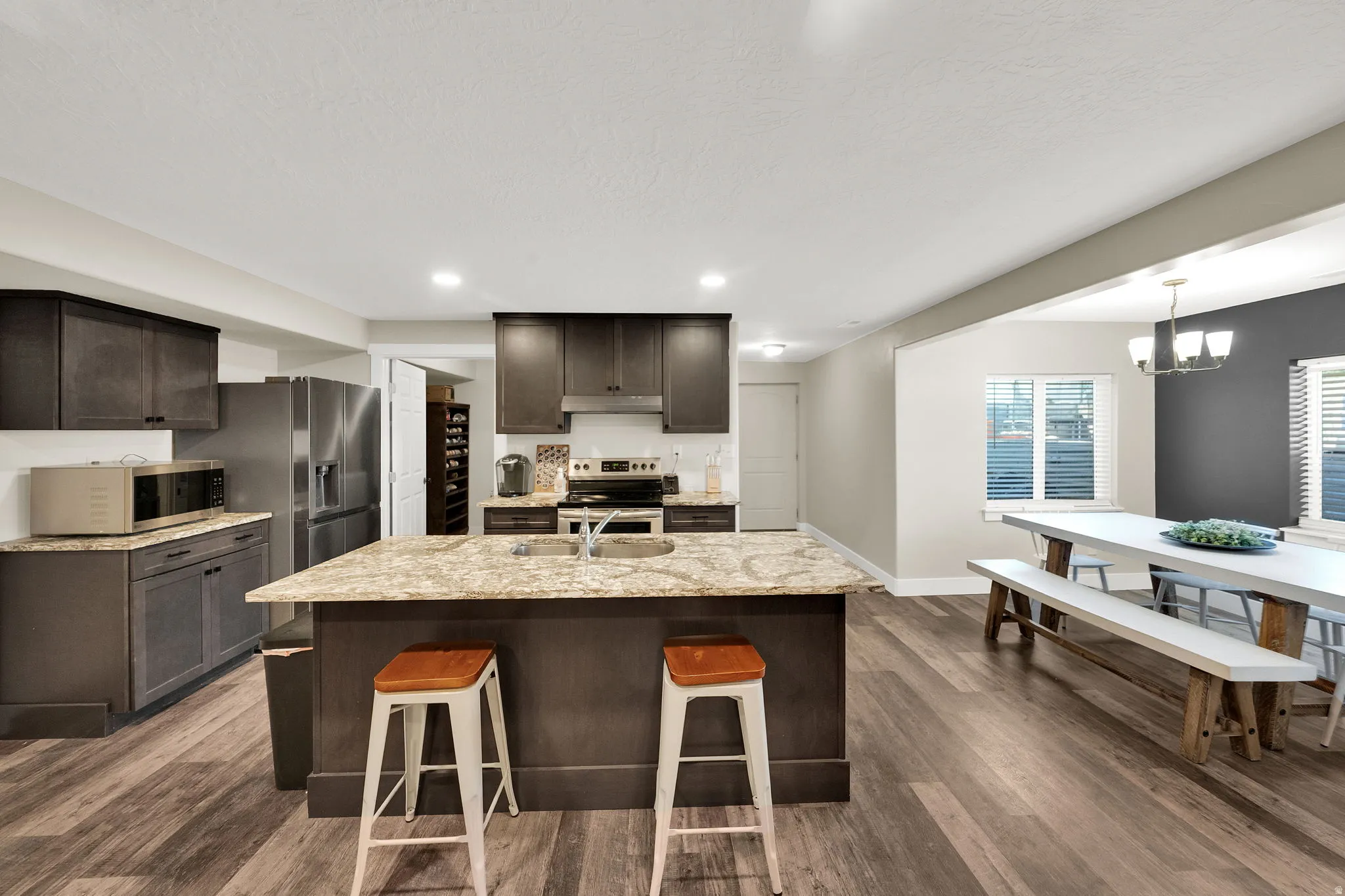 Open-concept kitchen featuring wood-finish flooring, dark wood cabinetry, stainless steel appliances, a center island with countertop seating, and recessed lighting