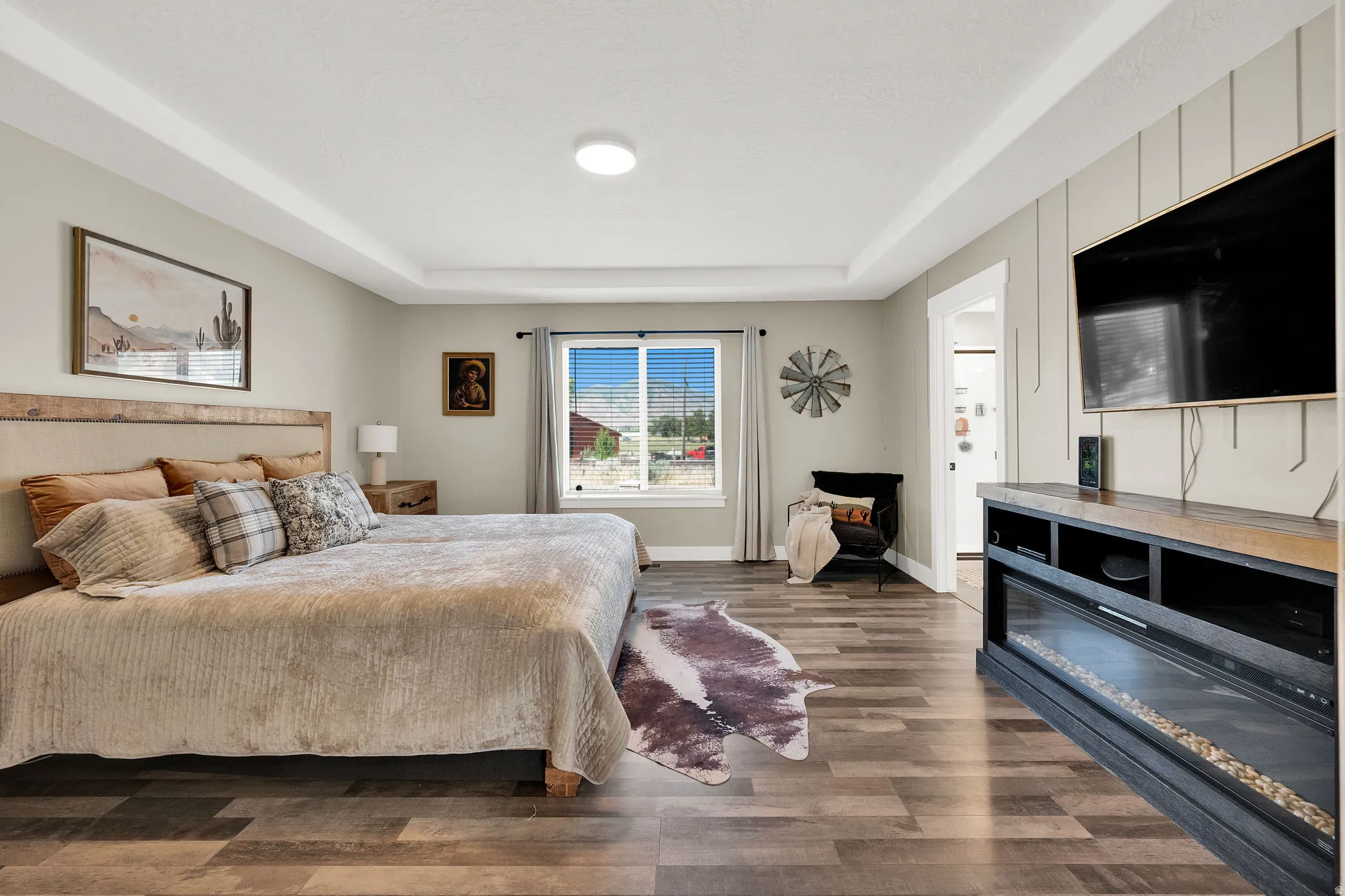 Spacious room featuring wood-finish flooring, tray ceiling, and a built-in media console with an integrated electric fireplace