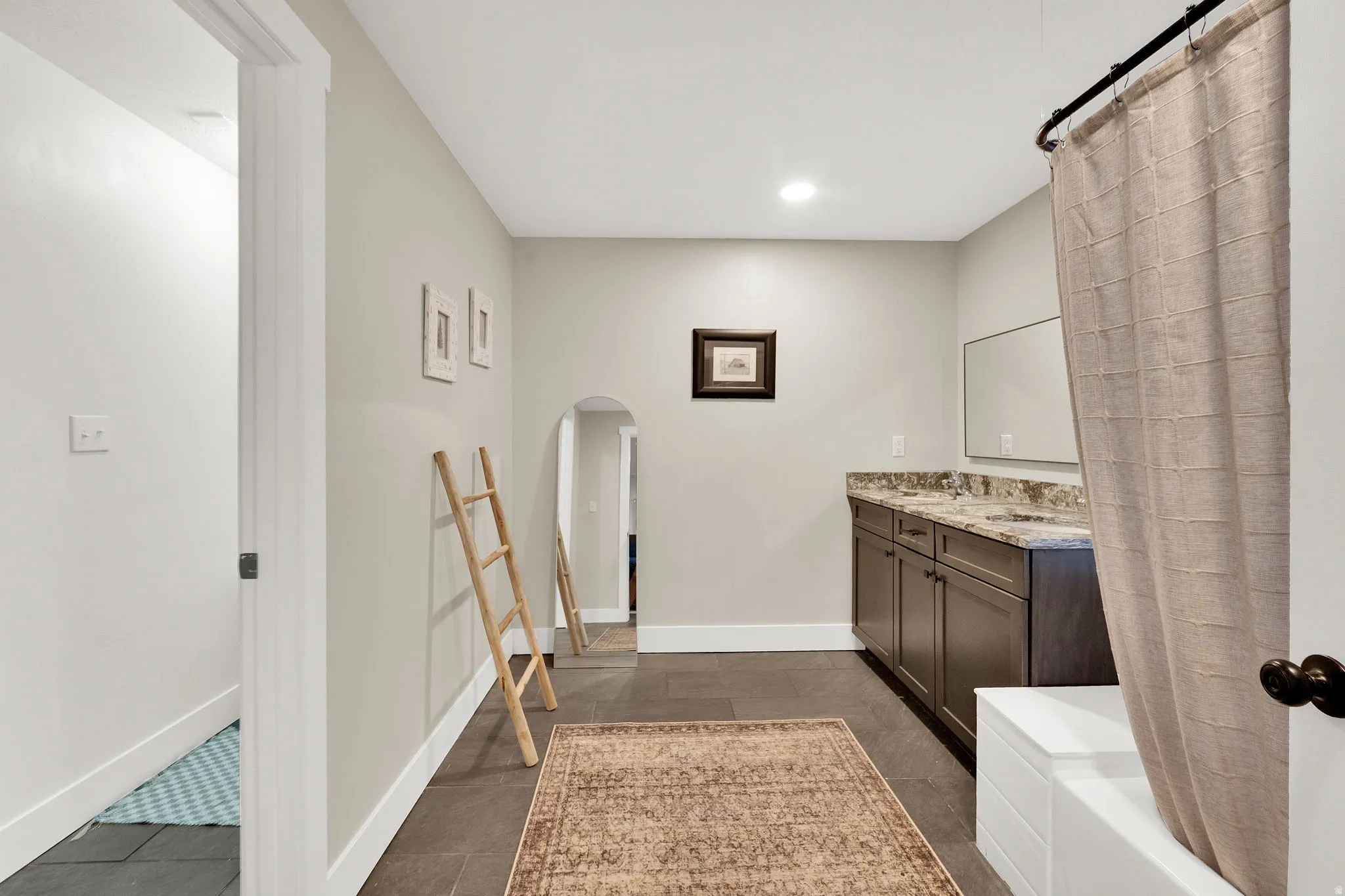 Bathroom featuring a dual vanity with a stone-finish countertop, dark wood cabinetry, and a built-in tub with shower curtain rod