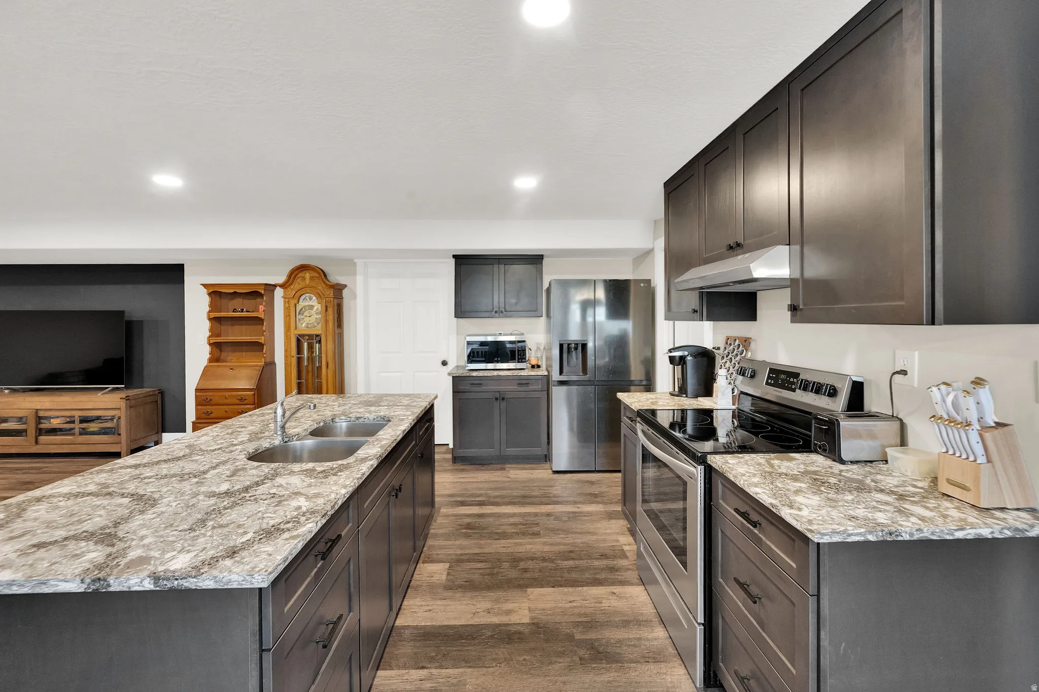 Kitchen featuring dark wood cabinetry, a large kitchen island with a double basin sink, stainless steel appliances, and wood-finish flooring