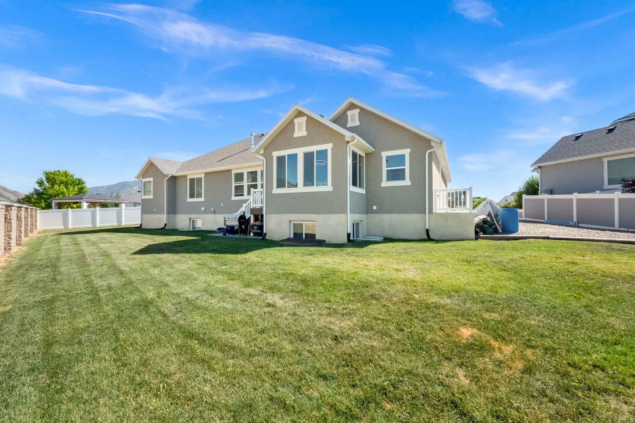 Expansive backyard with a manicured lawn, partial stone fence, and white vinyl fencing