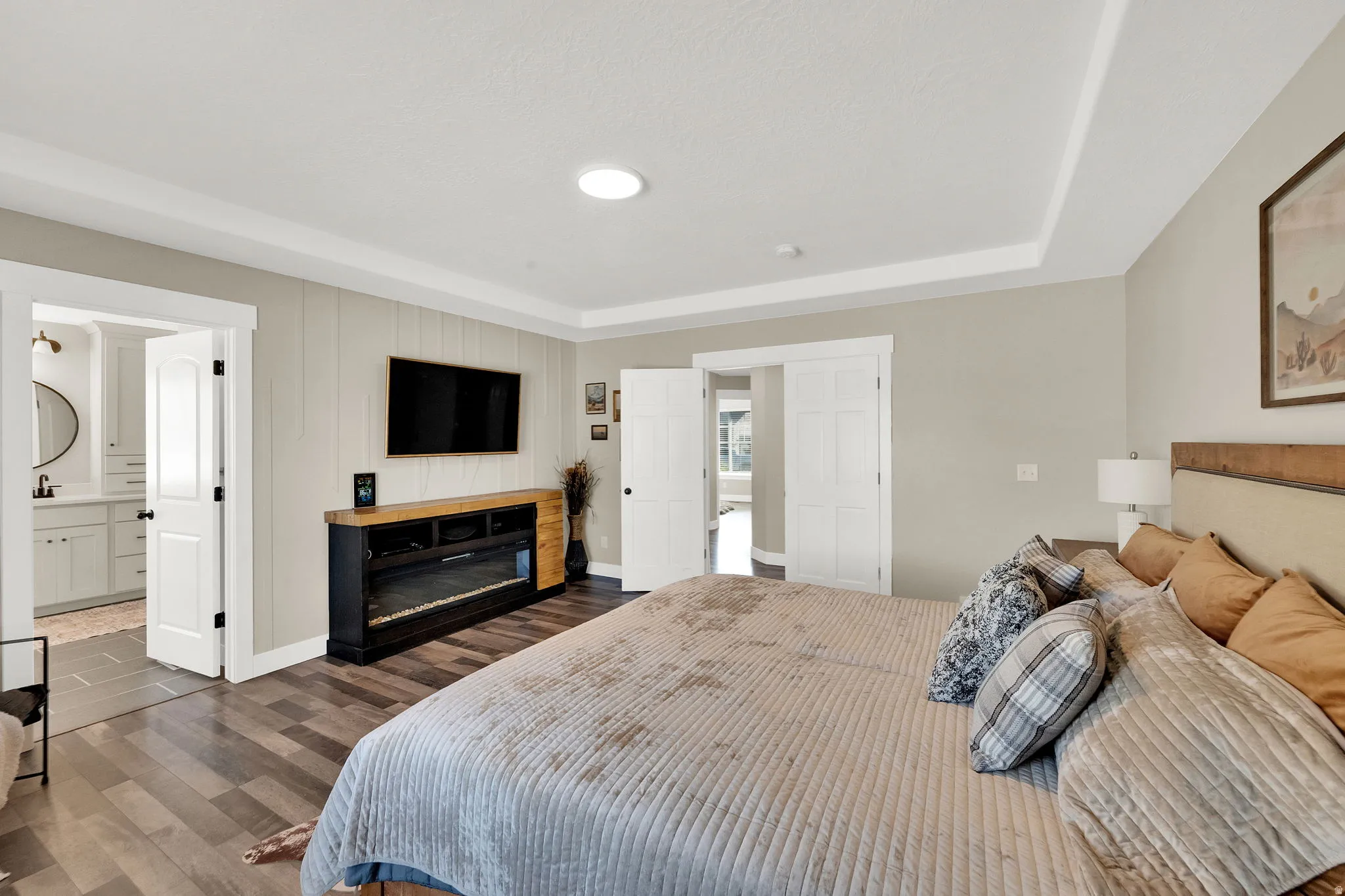 Spacious bedroom featuring wood-finish flooring, a built-in electric fireplace unit, and a tray ceiling