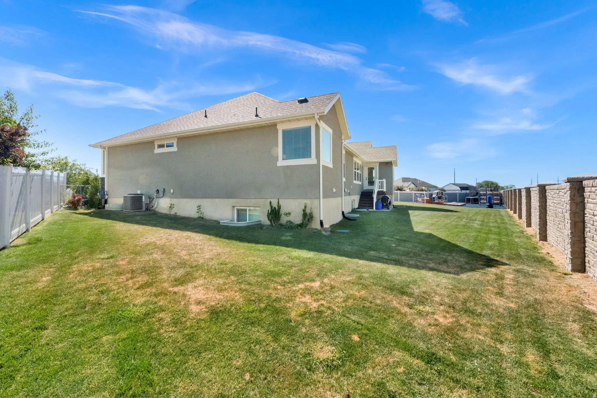 Expansive backyard featuring a partial white vinyl fence and a stone retaining wall