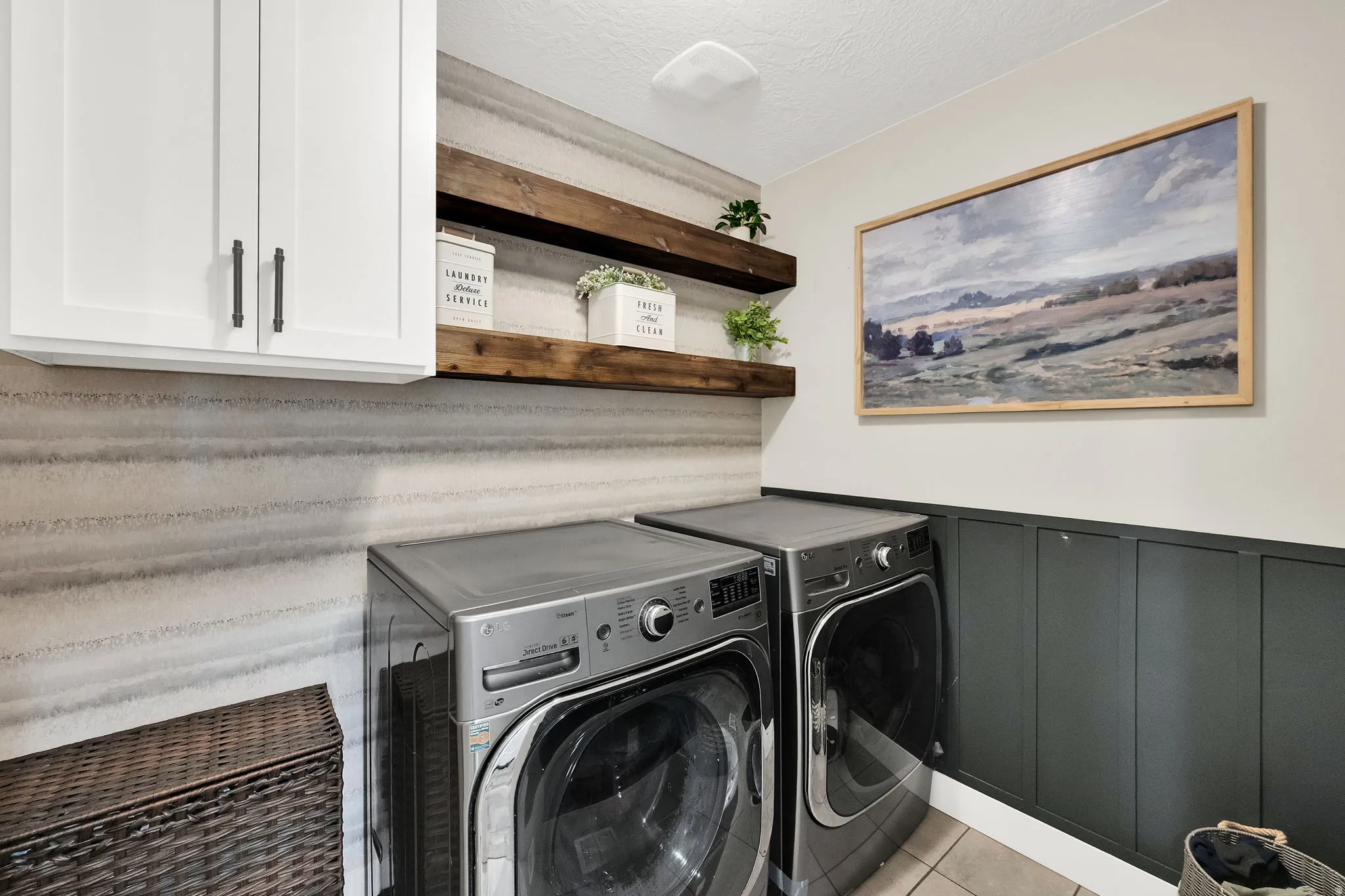 Dedicated laundry space featuring white shaker cabinetry with dark hardware, natural wood floating shelves, and a gray panel accent wall