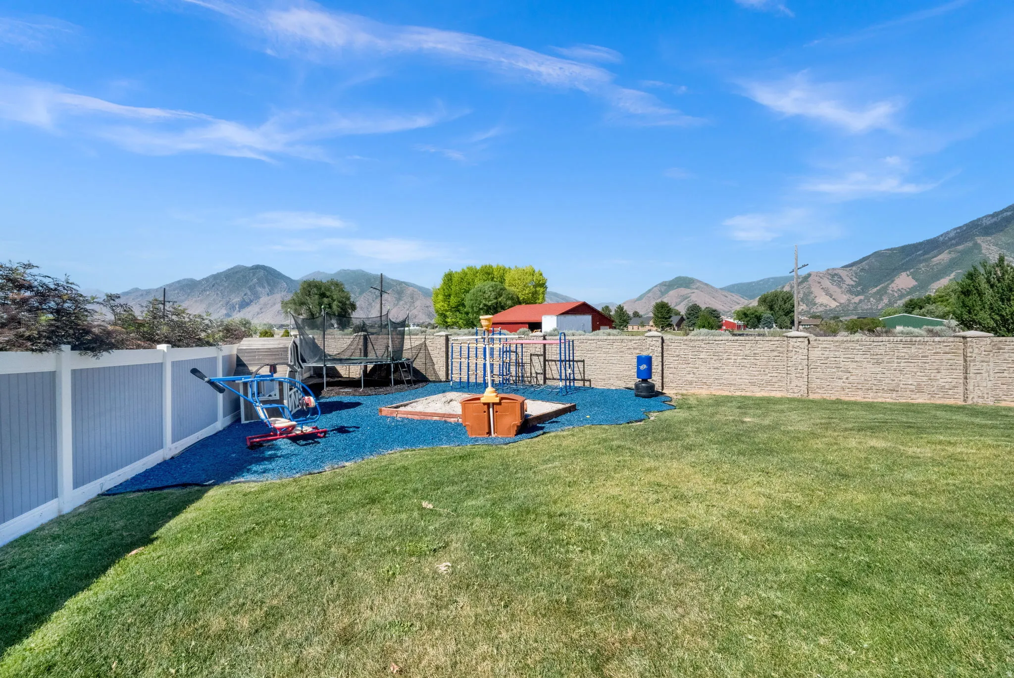 Expansive lawn with a dedicated play area featuring blue rubber mulch, a sandbox, and various playground equipment