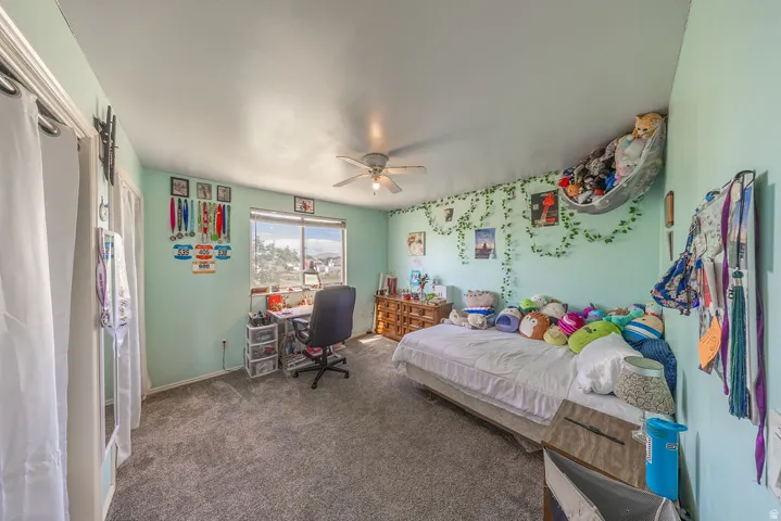 Bedroom featuring a ceiling fan, window with exterior views, light-colored walls, and gray carpet flooring