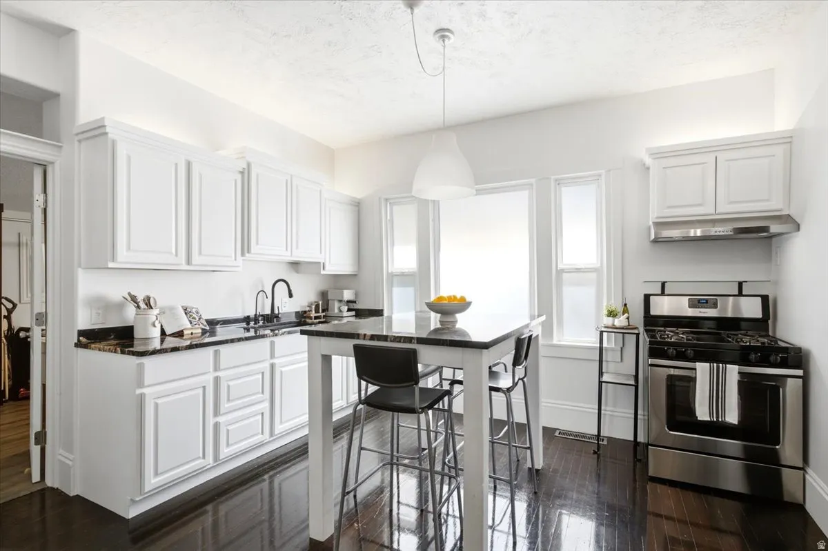 Kitchen featuring Original Hardwood dark wood-finish flooring, white cabinetry, dark countertops, a stainless steel gas range, and a central island with seating