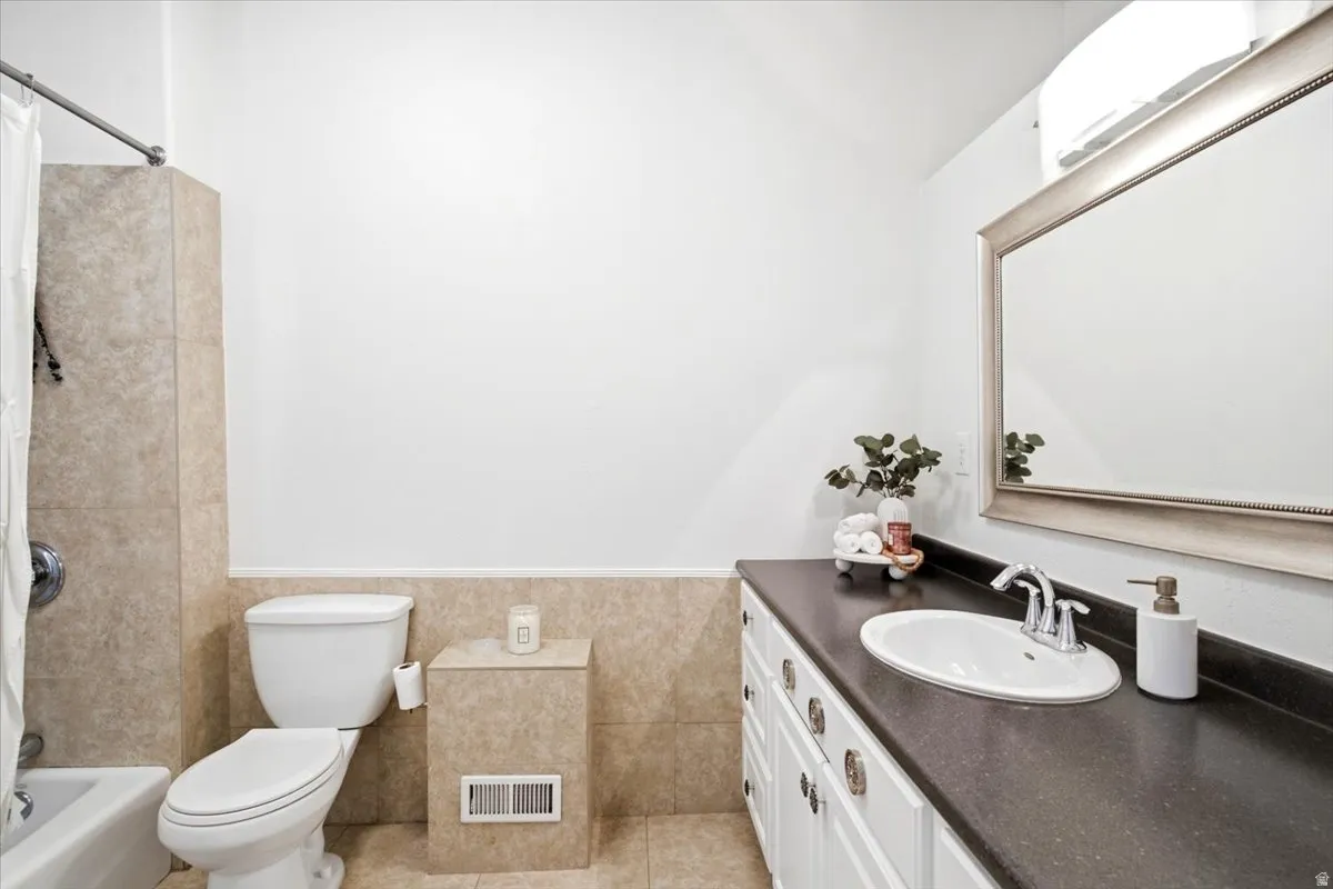 Bathroom featuring a white bathtub with a shower, a toilet, and a vanity with a dark countertop