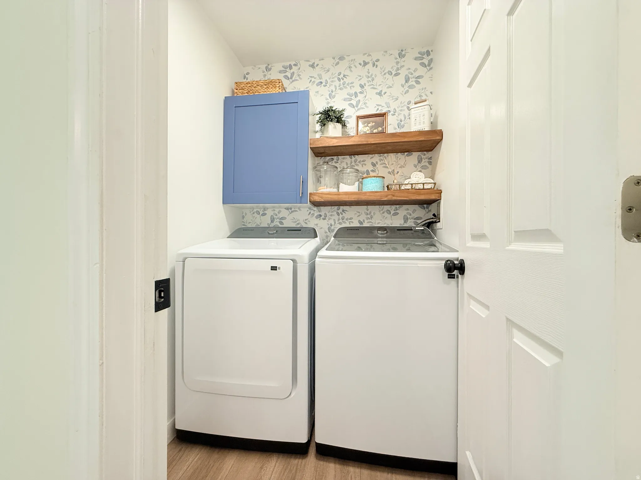 Dedicated laundry area featuring wood-finish flooring, a blue wall cabinet, and two floating wood shelves