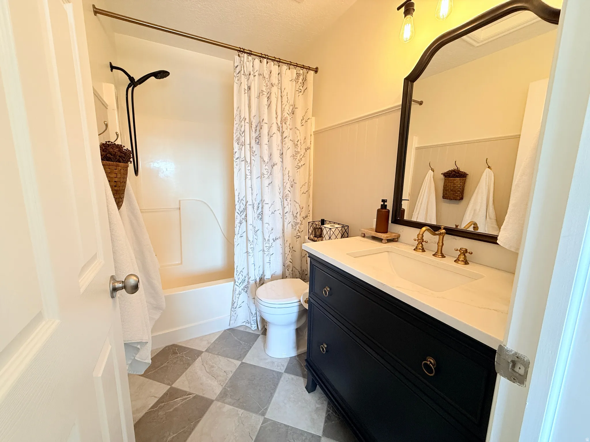 Bathroom featuring a dark vanity with a white countertop, an arched mirror, gold-tone fixtures, and checkerboard floor tiling