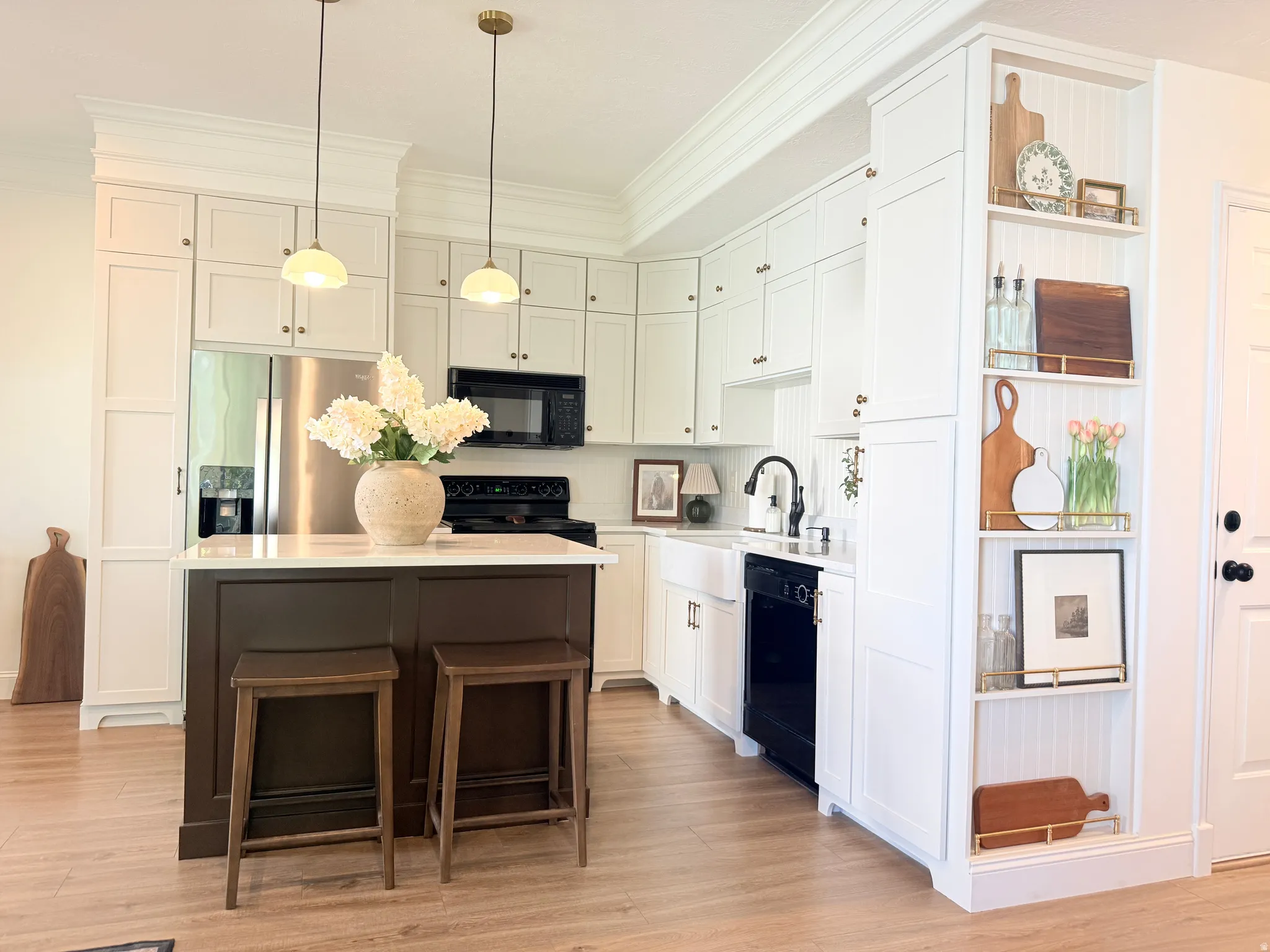 Kitchen featuring white shaker cabinetry, an island with a dark wood-finish base and light countertop, stainless steel refrigerator, black appliances, and wood-finish flooring