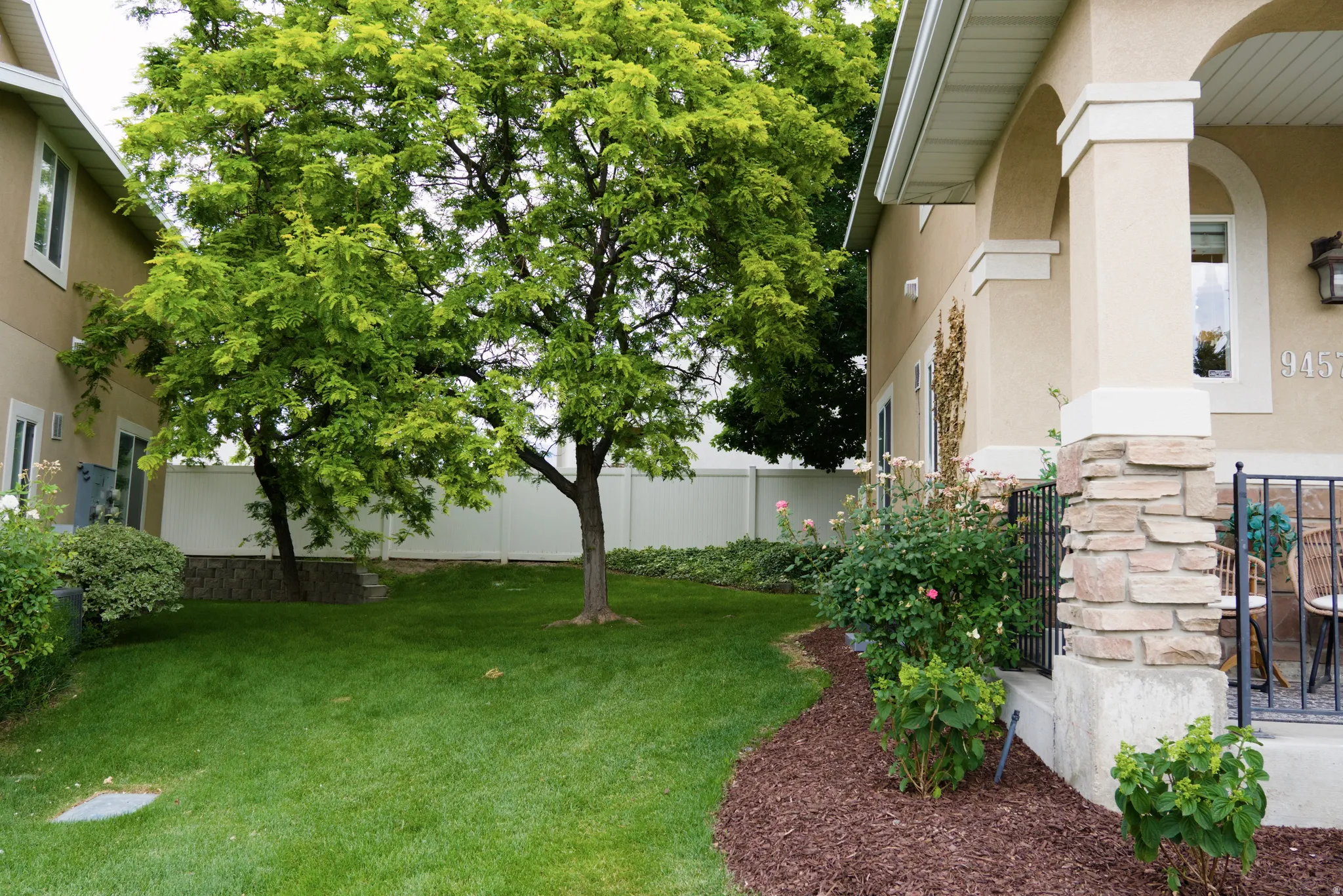 Expansive green lawn with mature trees and a white privacy fence
