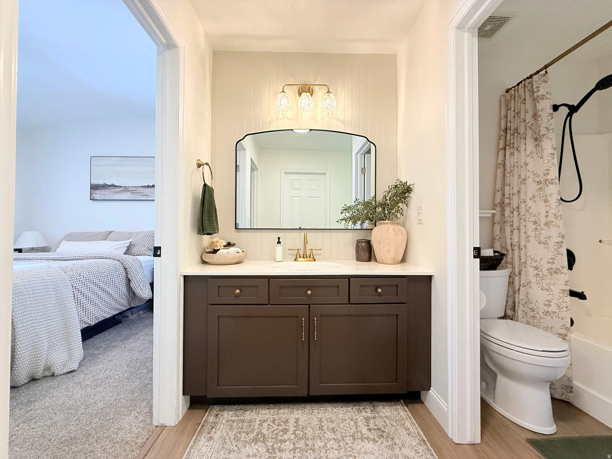 Bathroom vanity featuring a dark wood-finish cabinet with brass hardware, a light-colored countertop, and a contemporary arched mirror