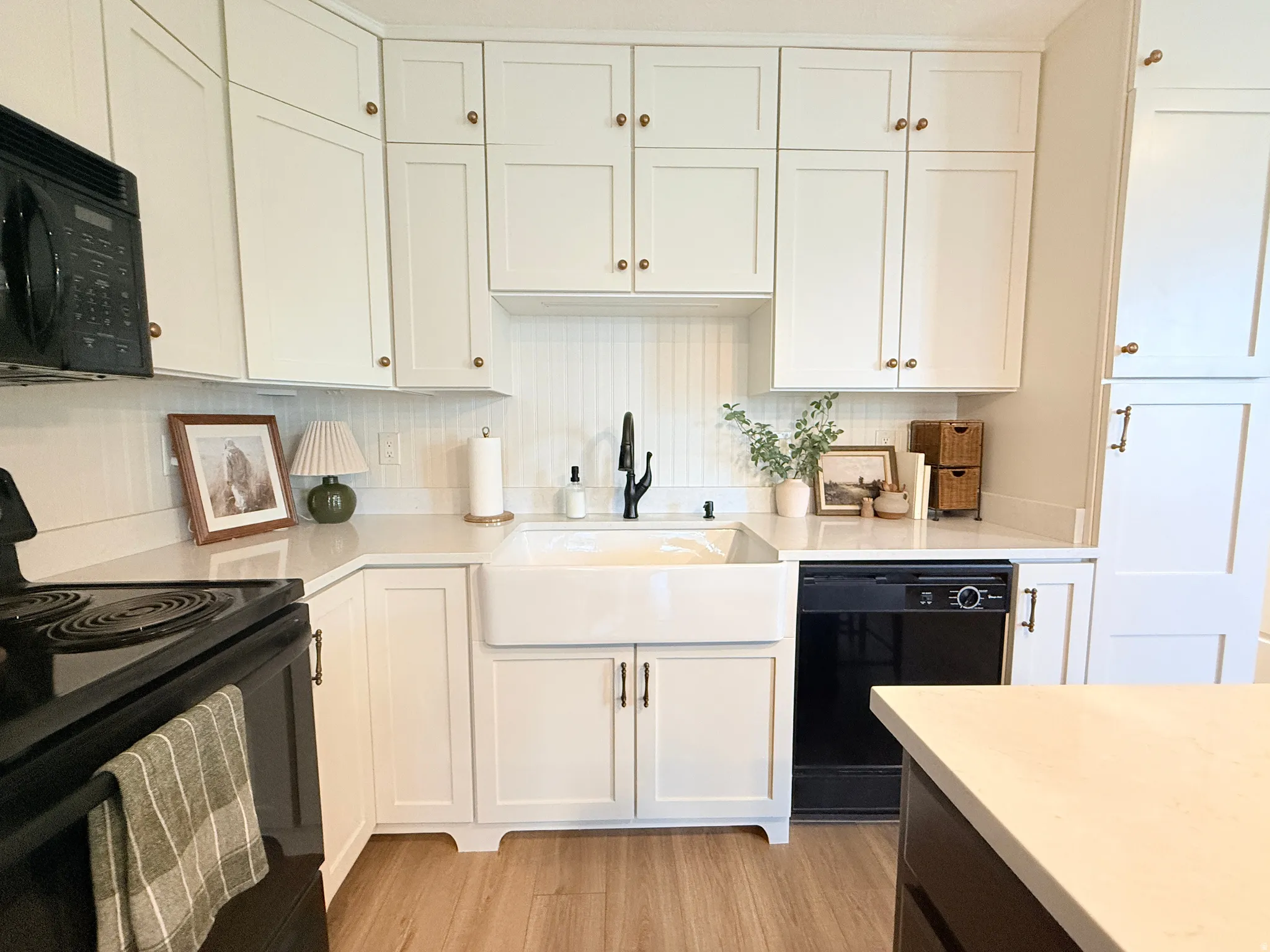 Kitchen featuring white shaker cabinetry, an apron-front sink with a matte black faucet, and beadboard backsplash