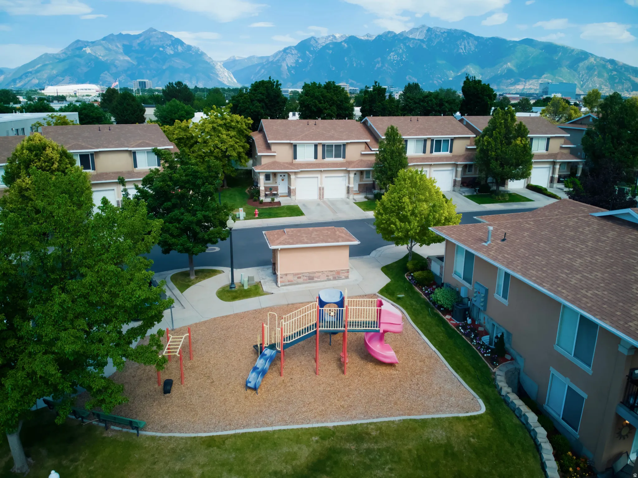 Community playground featuring multiple slides and climbing structures on a bark-mulch surface, bordered by green lawn and mature trees