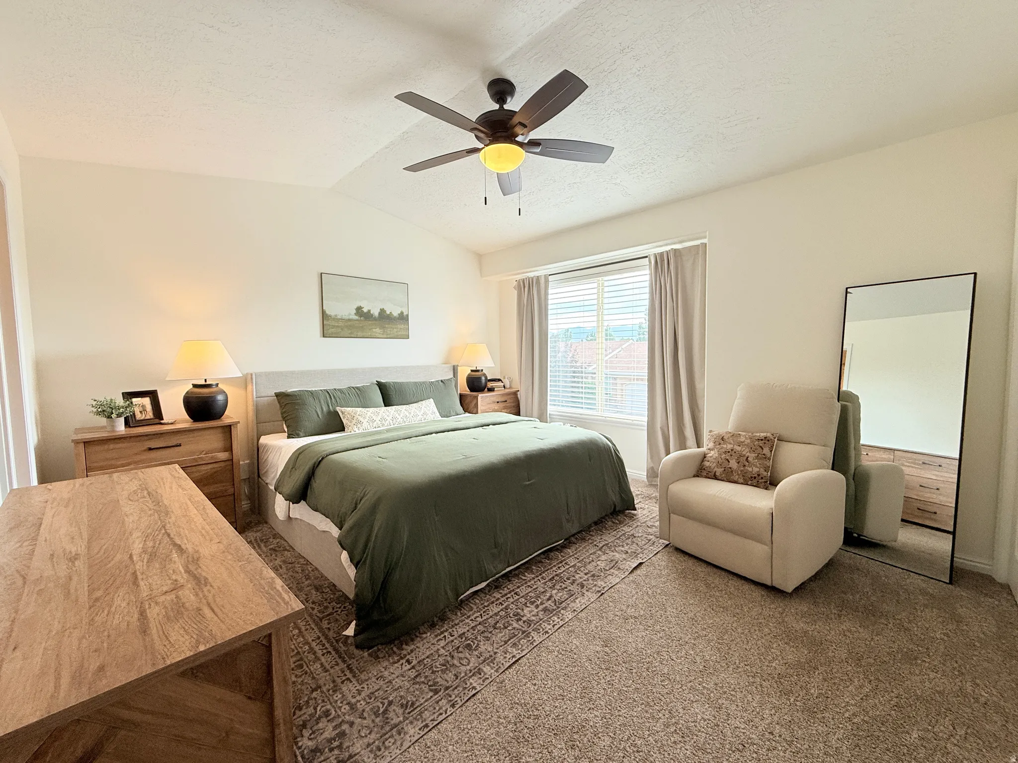Vaulted ceiling bedroom with a ceiling fan light fixture, window with blinds and drapes, and neutral tone carpet flooring