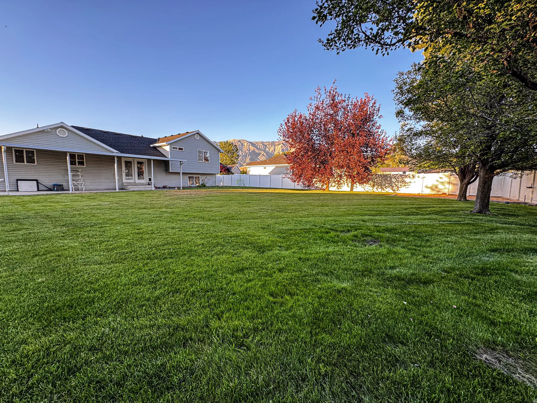 Expansive green lawn with mature trees and a white privacy fence, featuring a backdrop of distant mountains