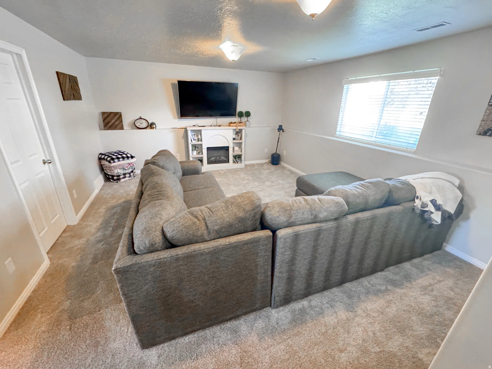Carpeted room featuring light gray walls, a built-in electric fireplace with shelving, and a large window with blinds