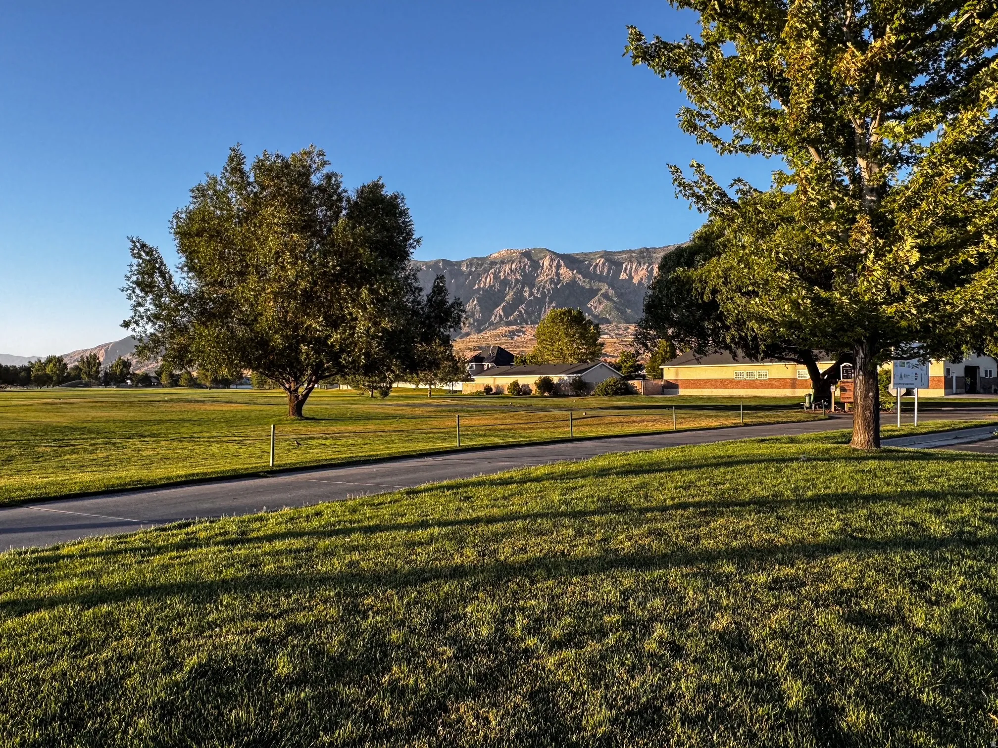 Expansive green space featuring a paved path and mature trees