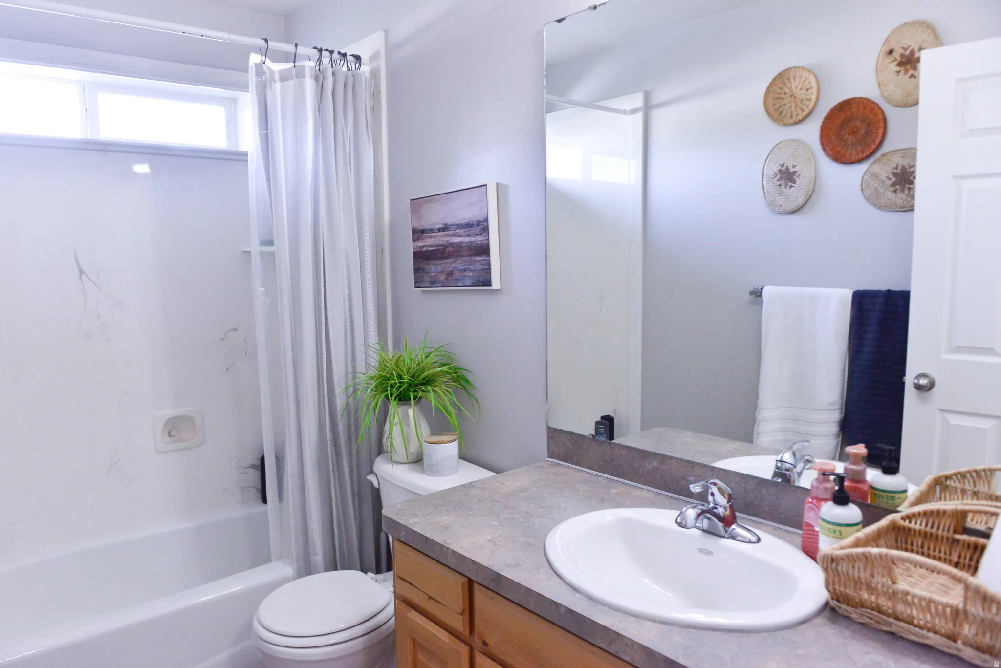 Bathroom featuring a white shower-tub combination with a window, a white toilet, and a vanity with an integrated sink and wood-finish cabinetry