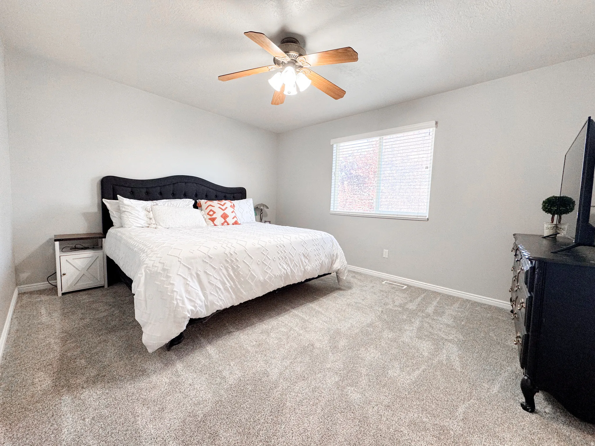 Spacious room with light gray walls, textured gray carpeting, and a wood-finish ceiling fan with integrated lighting