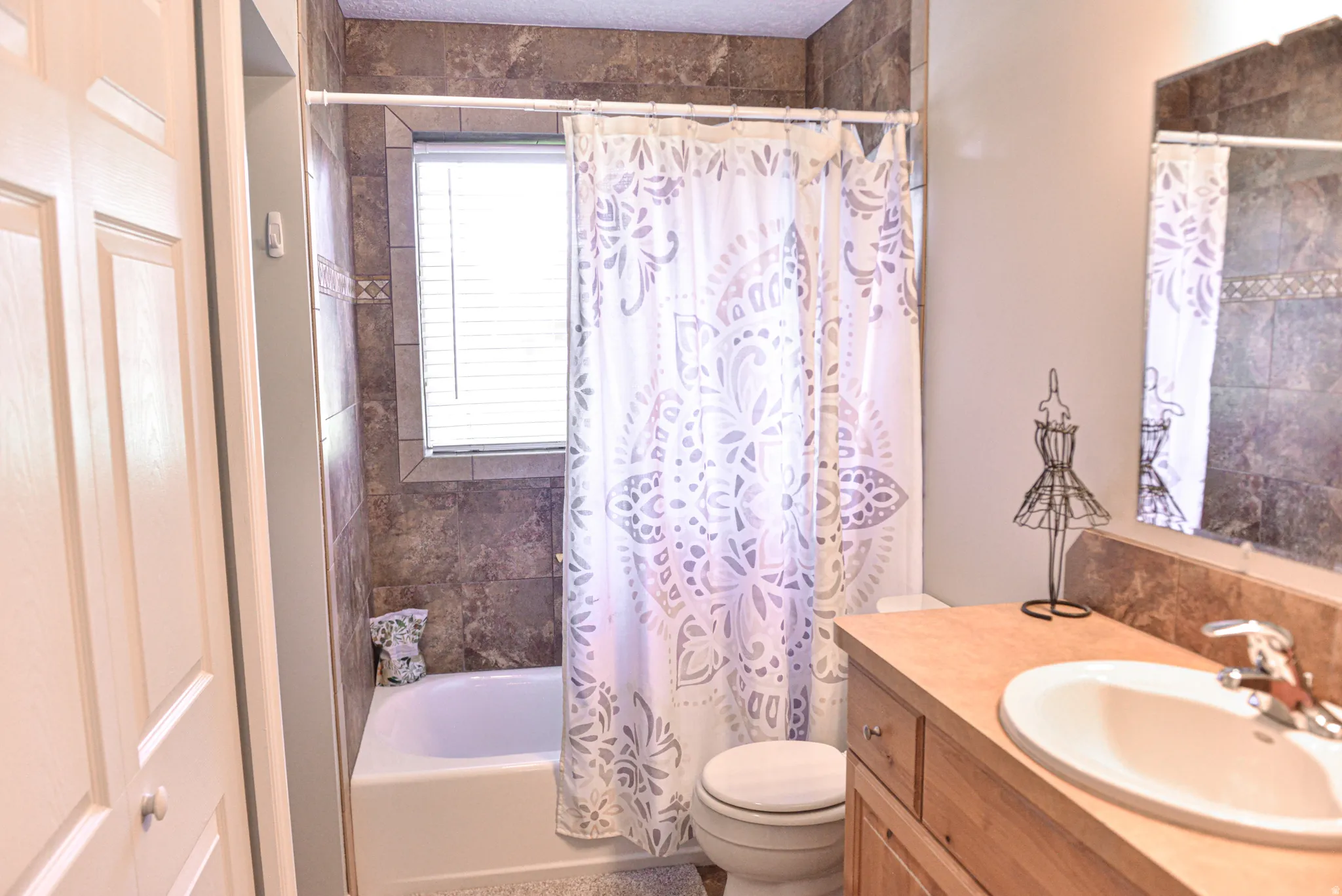 Bathroom featuring a tub/shower combination with full-height tile surround and a window with blinds