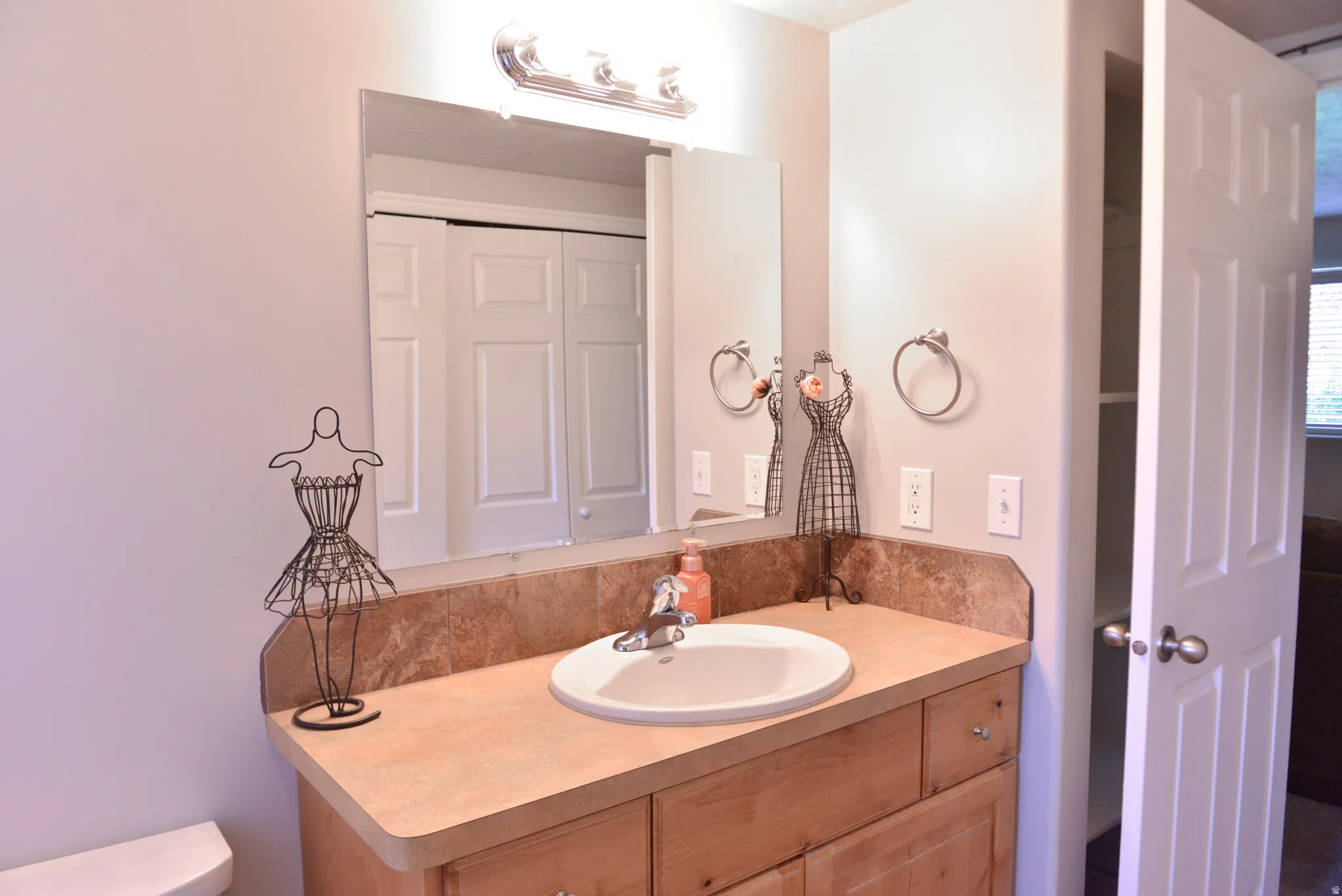 Bathroom vanity featuring a single basin sink, light-toned countertop with a matching backsplash, and wood-finish cabinetry