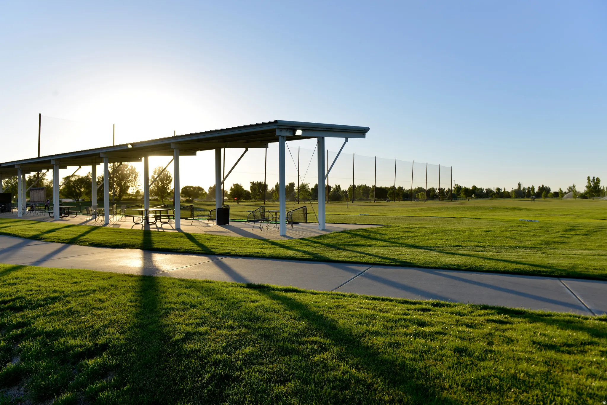 Shaded outdoor structure with a metal roof and support beams overlooking an expansive green field