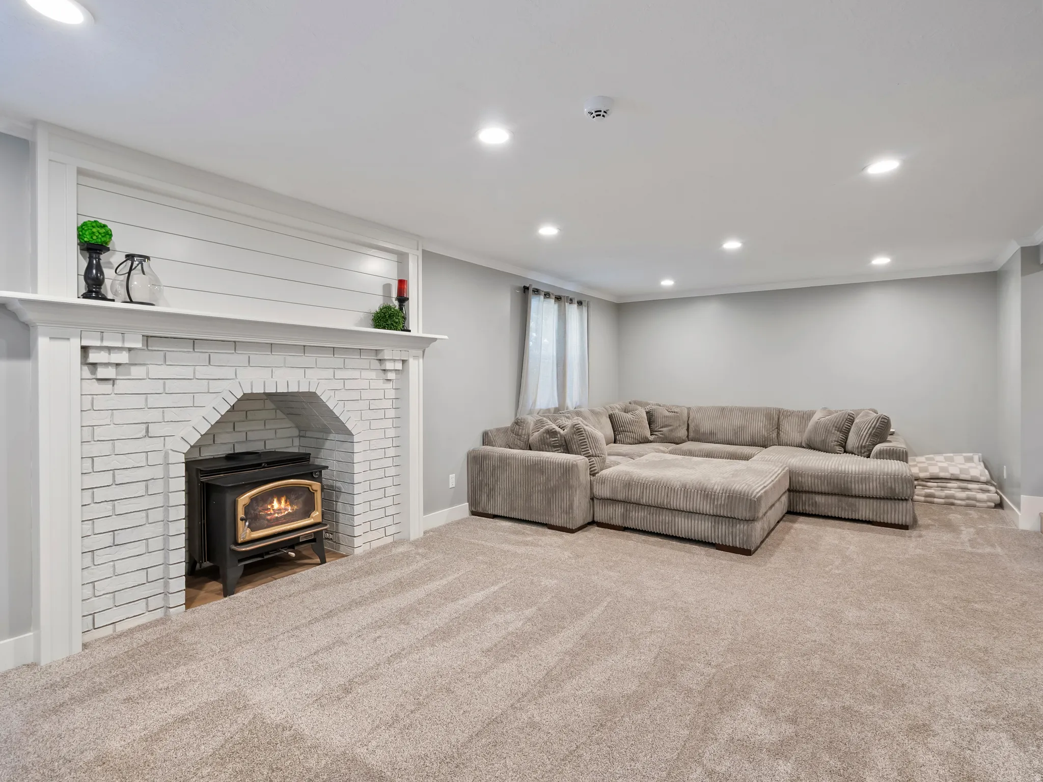 Finished lower level featuring a white painted brick fireplace with a wood-burning stove insert, shiplap detailing, and recessed lighting
