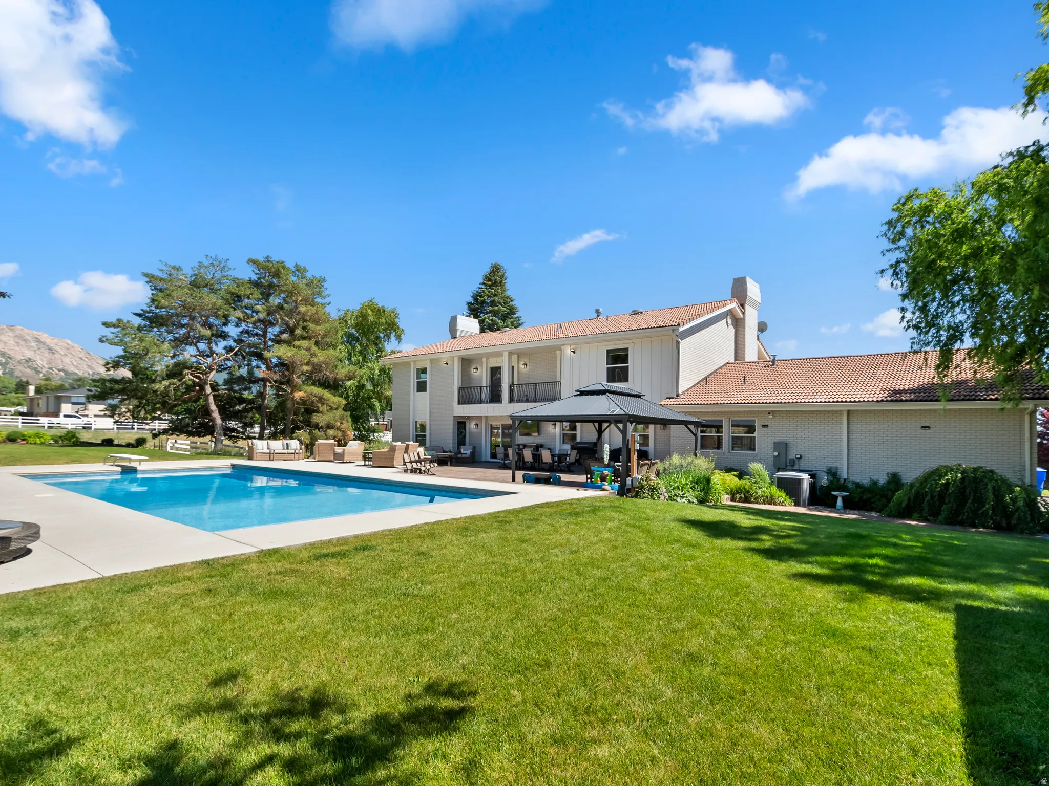Expansive backyard featuring an in-ground pool with a diving board, surrounding concrete patio, and a covered gazebo