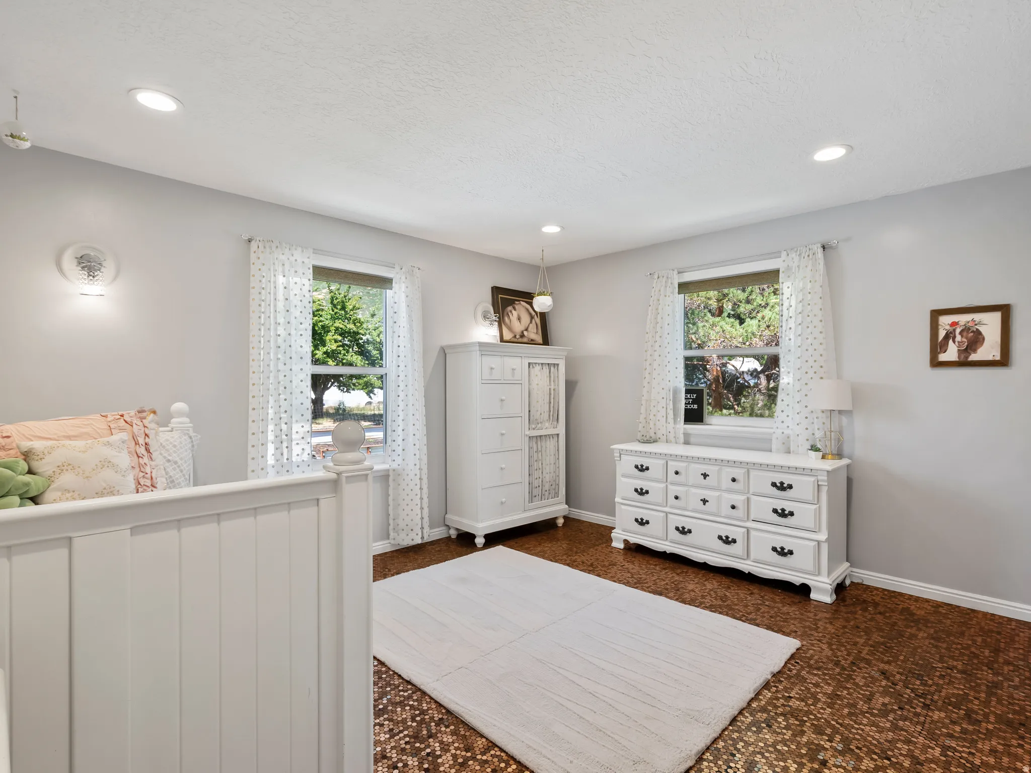Recessed lighting illuminates the room, featuring a unique textured flooring, two windows with natural light, and two wall-mounted sconces