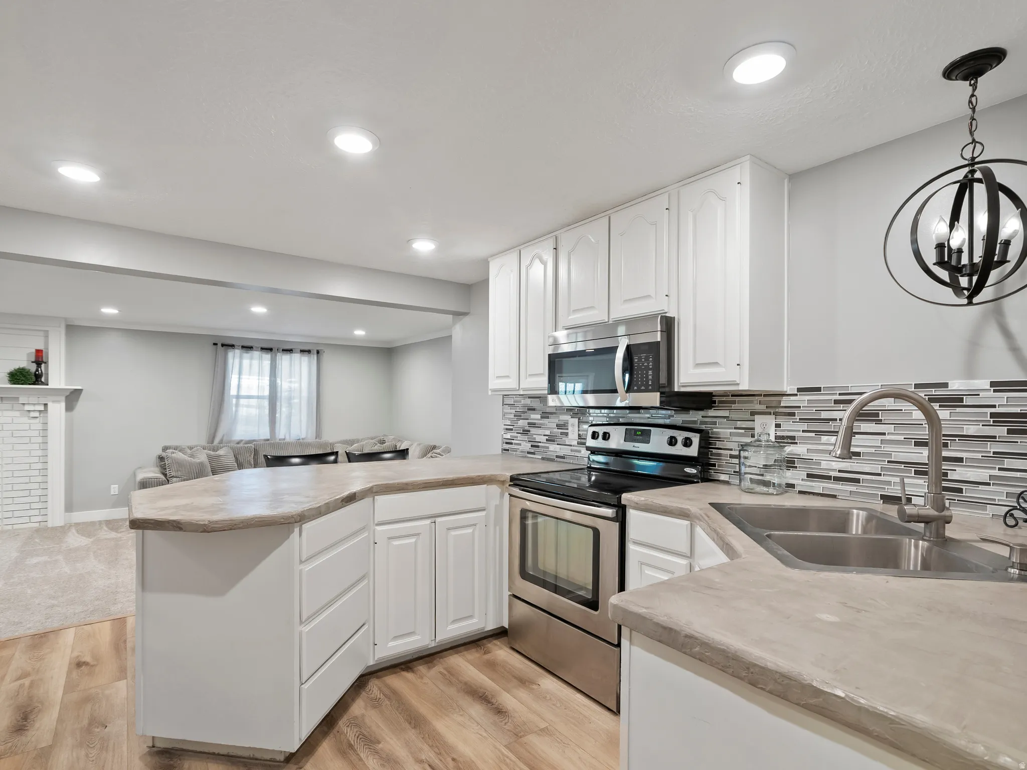Modern kitchen featuring white cabinetry, stainless steel appliances, a mosaic tile backsplash, and a double basin sink with a gooseneck faucet