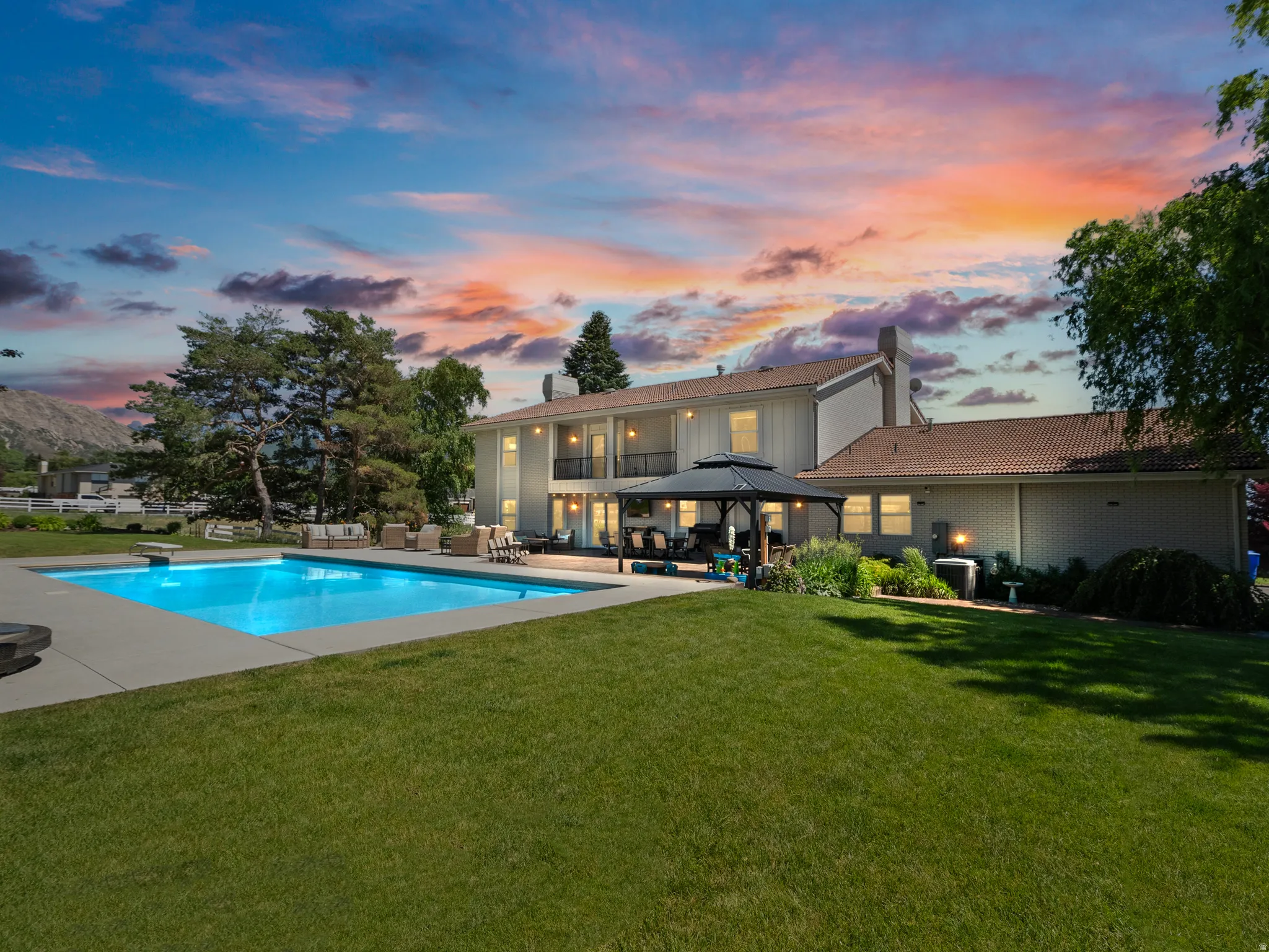 Expansive backyard featuring an in-ground swimming pool with an integrated diving board, a patio area with a built-in gazebo, and mature landscaping