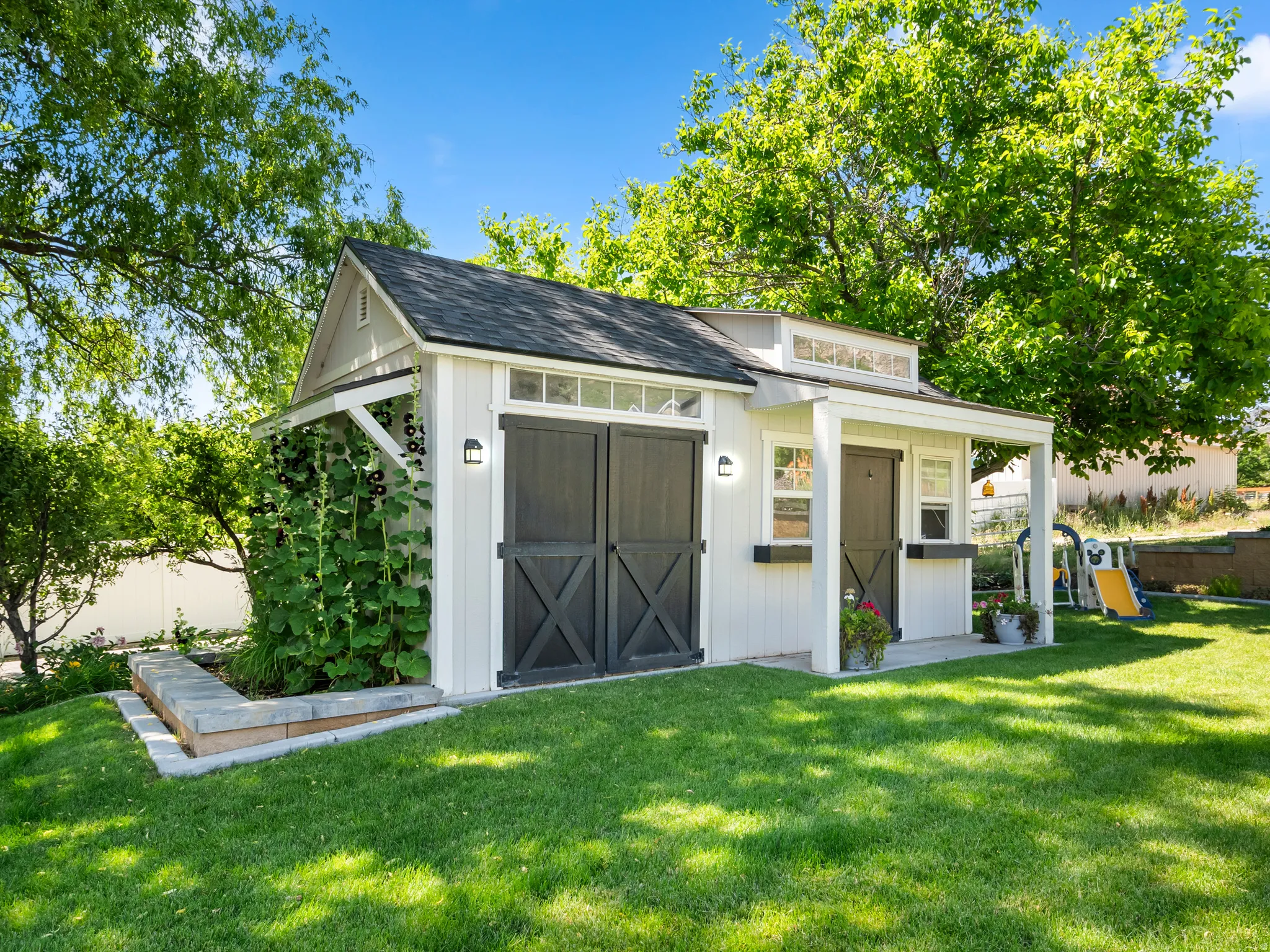 White-sided shed with dark barn doors, a covered porch, and a raised garden bed