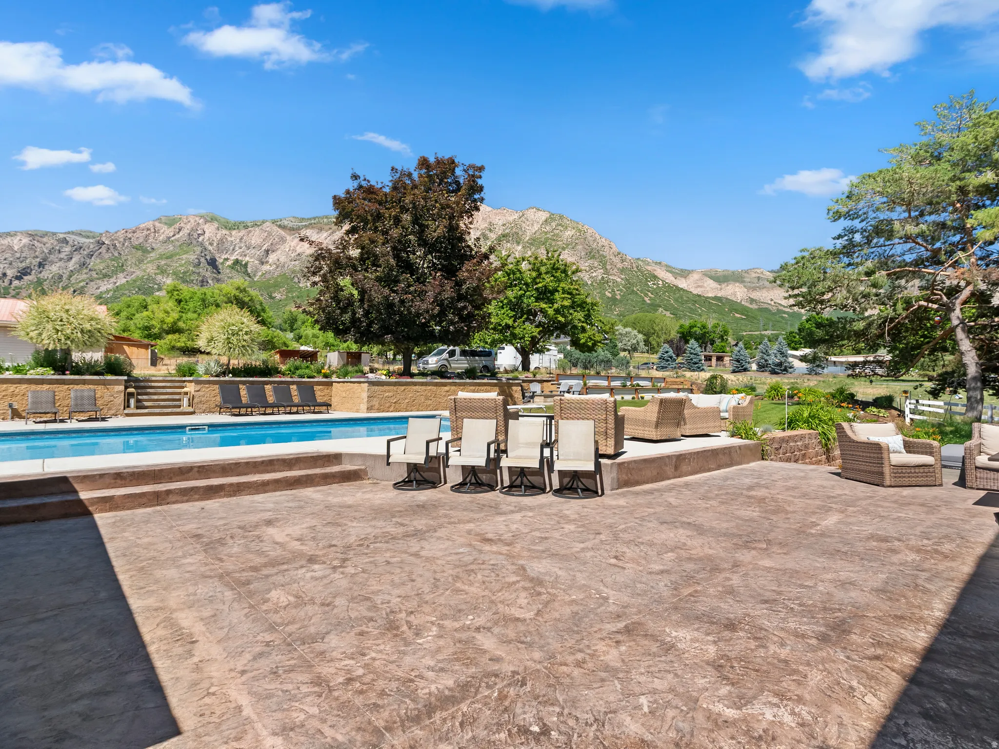 Expansive stamped concrete patio with a tiered design, featuring an in-ground swimming pool, stone retaining walls, and a mountain backdrop