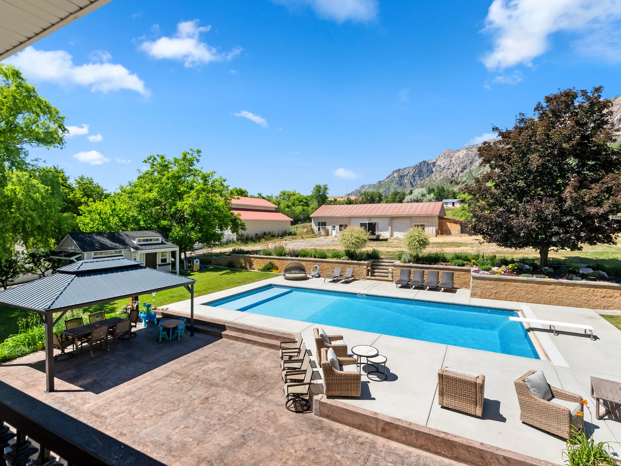 Expansive backyard featuring a rectangular swimming pool with diving board, a large stamped concrete patio, a built-in gazebo, and terraced landscaping with retaining walls