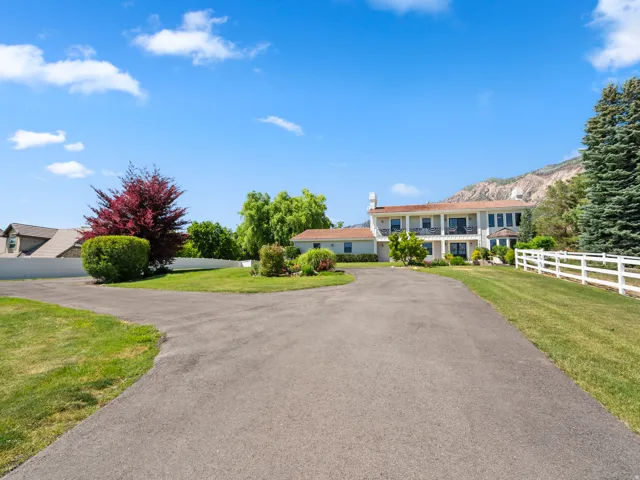 Paved driveway leading to a multi-level residence with a white post-and-rail fence